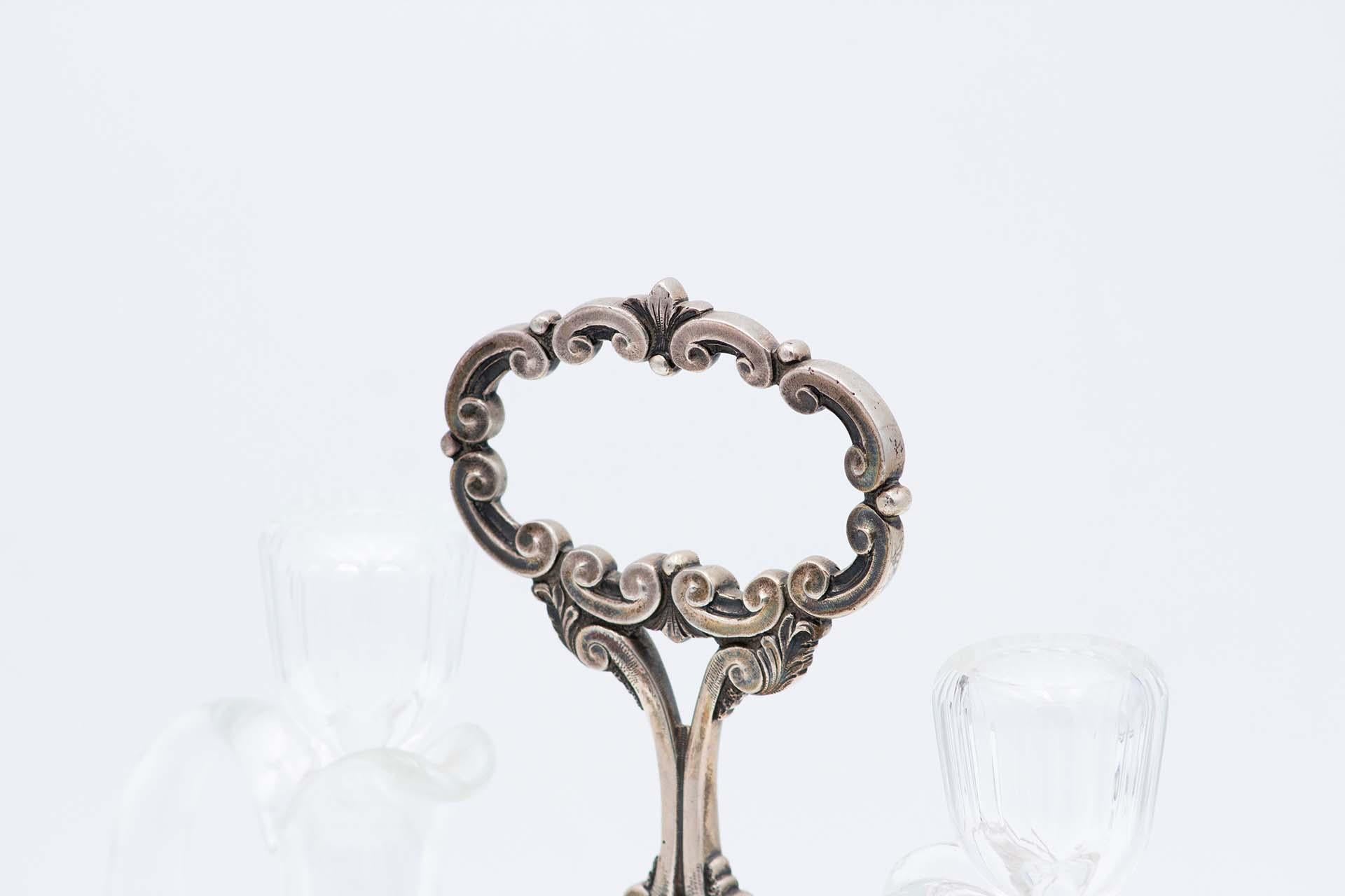 Description: Cruet with embossed and openwork silver structure on the stem and handle, smooth base with ornaments and resting on four feet. Metal: Silver. Origin: Portuguese. Mark: standing eagle. Weight: 1784.90 grams. Dimensions: 29.2cmx23.7cm.