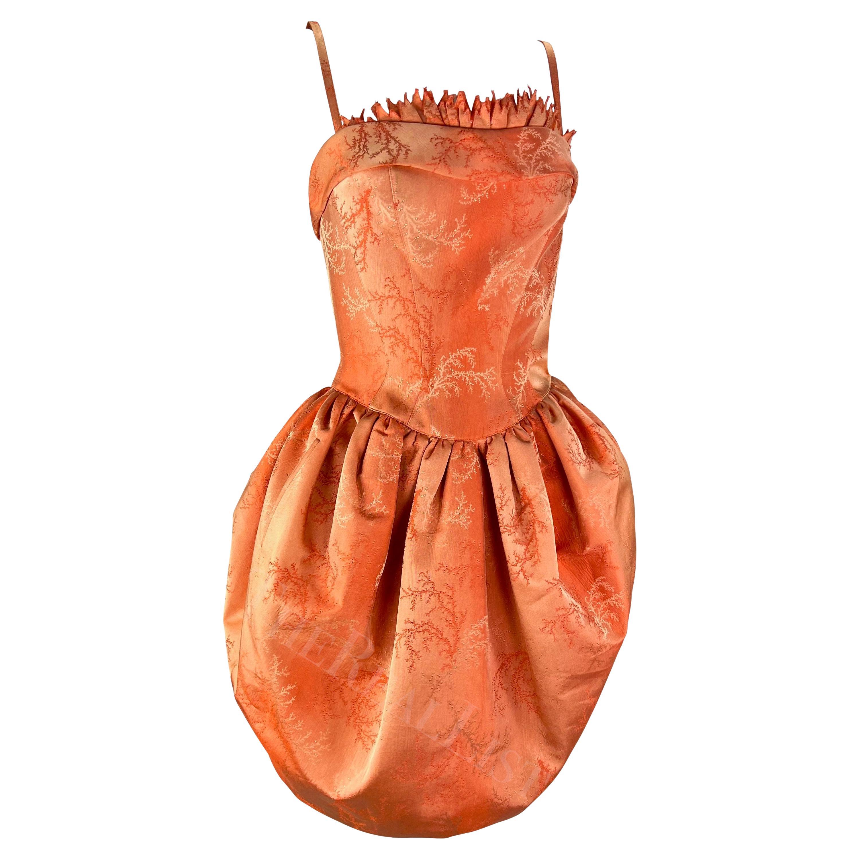 A rare sample from Thierry Mugler's Cruise 1999 collection, this striking coral orange mini dress features a voluminous skirt, fitted top, and spaghetti straps. Covered in a monochrome orange floral jacquard weave, this corseted mini dress is made