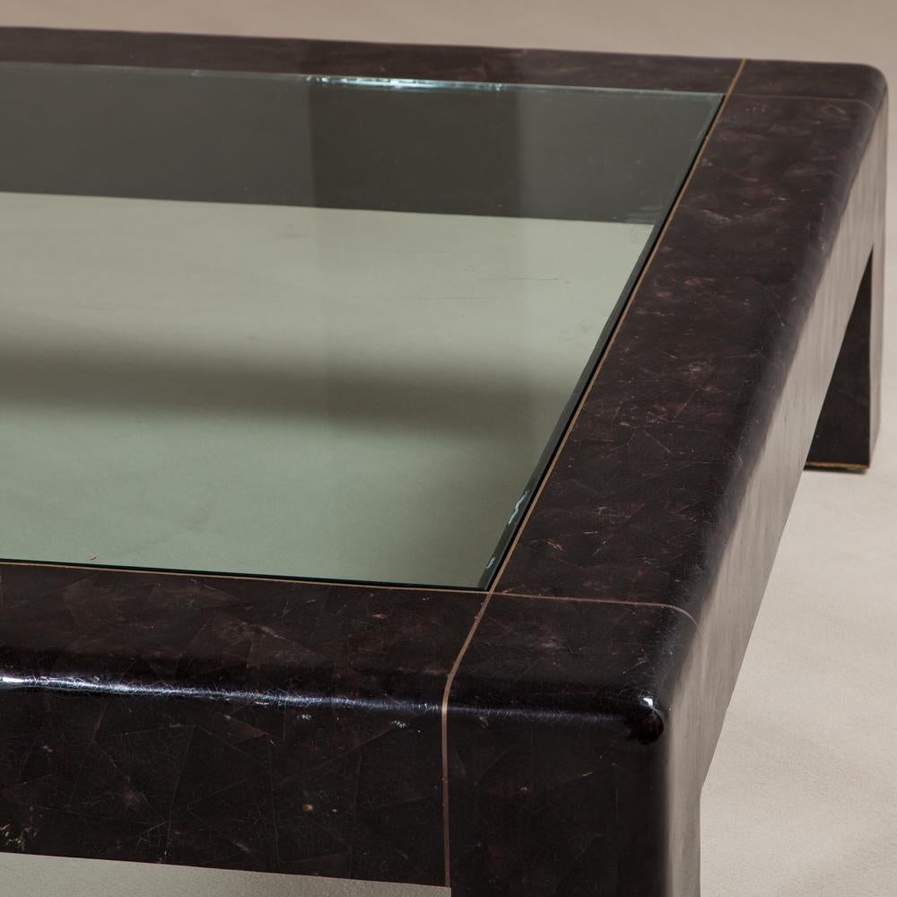 A large square crushed shell veneered coffee table by Karl Springer, in deep brown/purple and detailed with fine patinated brass inlay, retains Makers Mark, 1980s.

Karl Springer established a tiny workshop in Manhattan and started concentrating