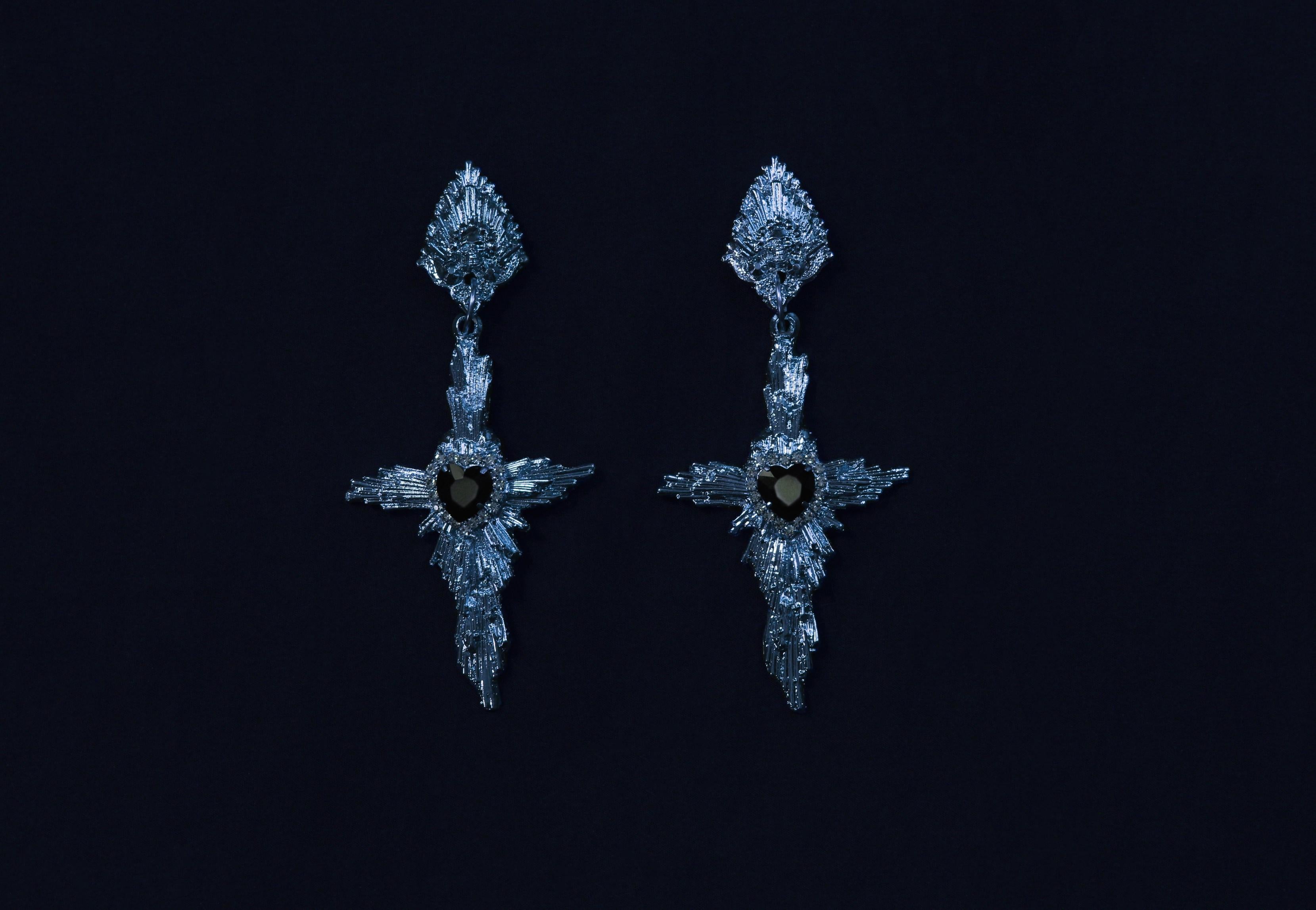 Crux Earrings by Angelis Blade

Delicate yet striking, the Crux earrings command attention through their powerful design. At their heart is a glass faceted heart jewel, symbolising both purity and passion, framed by rays that form a sacred cross.