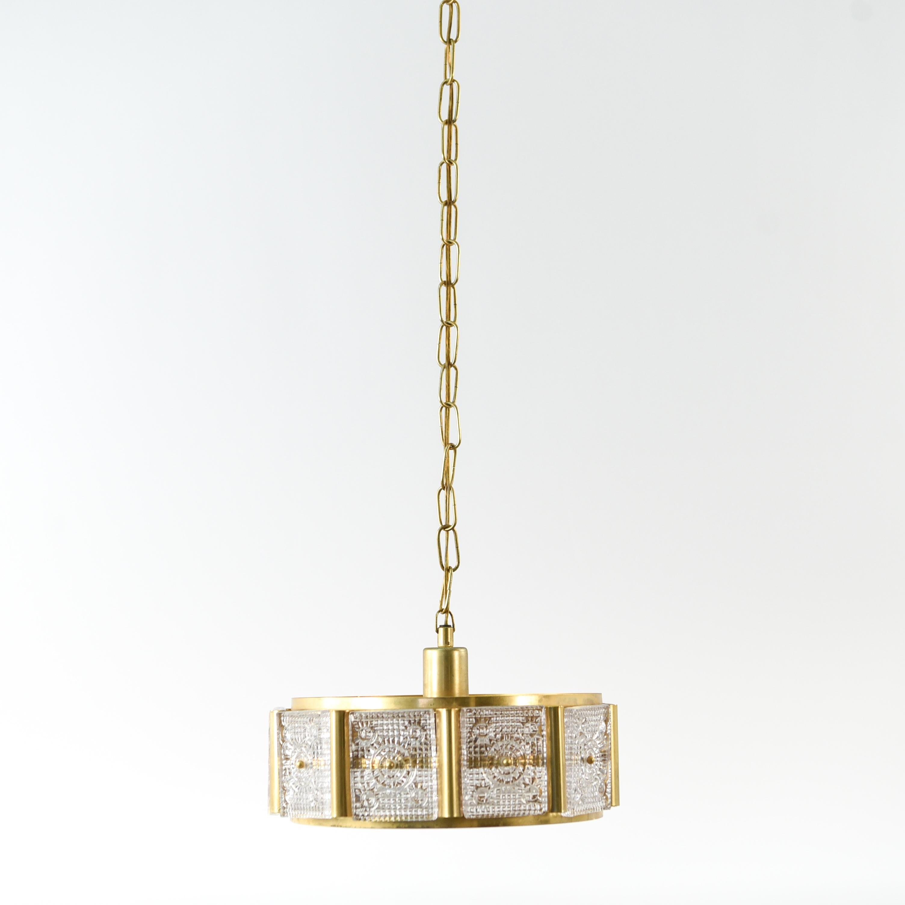 This crystal and brass pendant chandelier was designed by Carl Fagerlund for Orrefors, circa 1960s. This piece has beautifully designed crystal panels in a brass framework and is in a short cylindrical form, characteristic of most of Fagerlund's