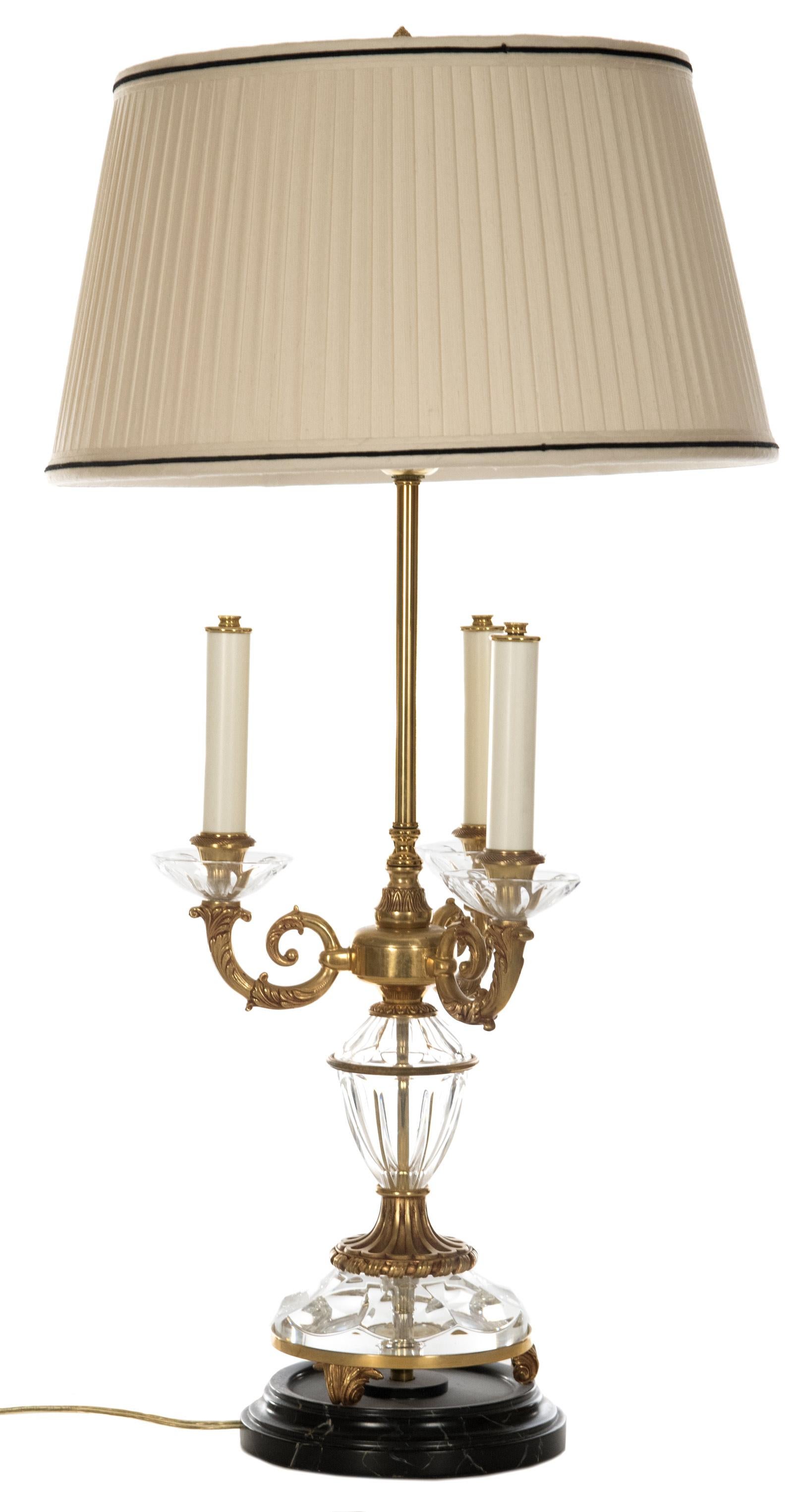 A faux candelabra table lamp of crystal and brass, three arms with chased detailing supporting candlestick forms, the thin brass stem supporting two lights within the drum shade, all raised on a round, variegated black and gold marble base.