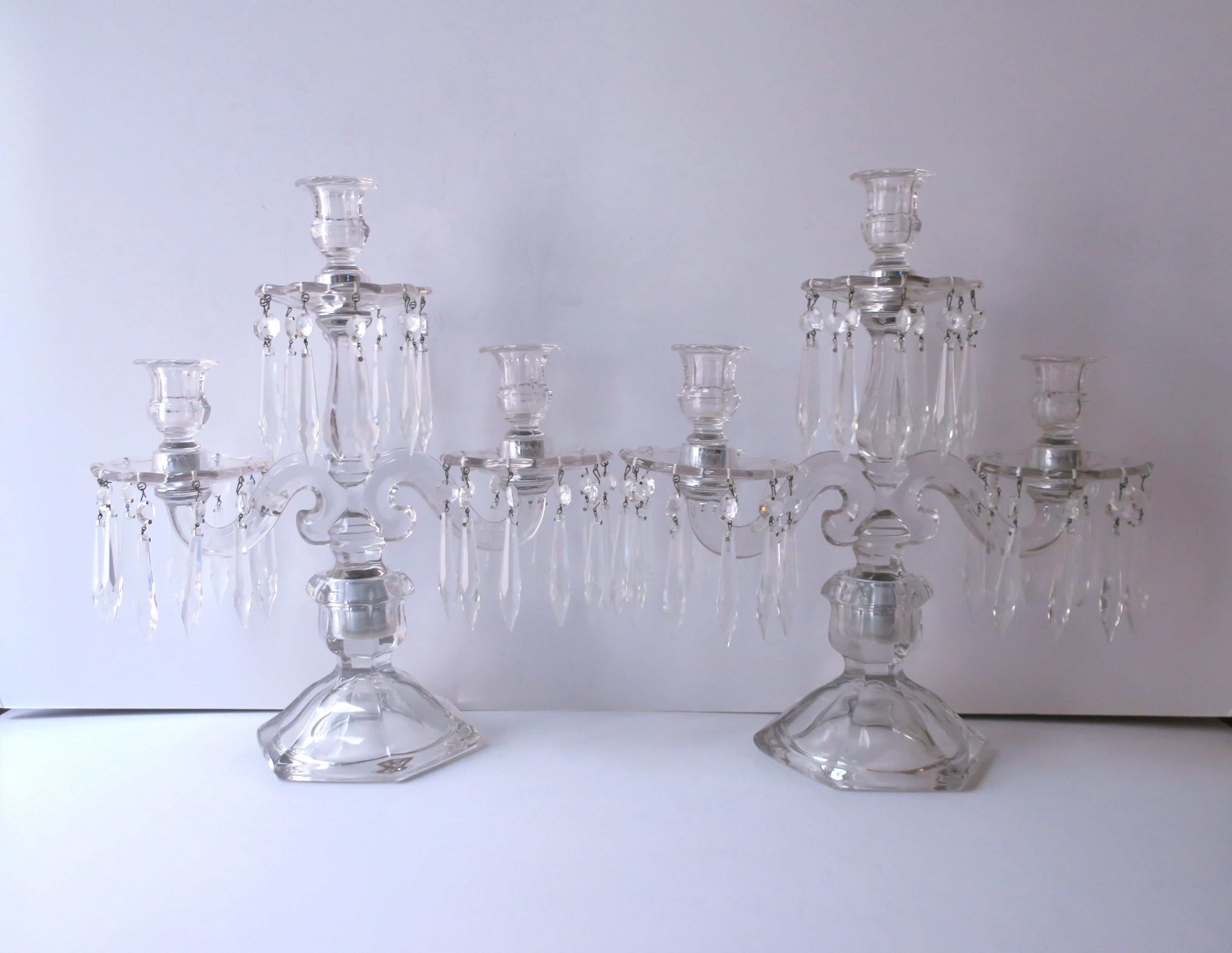 A beautiful pair of two arm, three light, transparent glass candelabras with crystal drop prisms and removable bobeches, circa mid-20th century. A bobeche is a glass collar on a candle socket to catch drippings and/or to hold suspended crystal