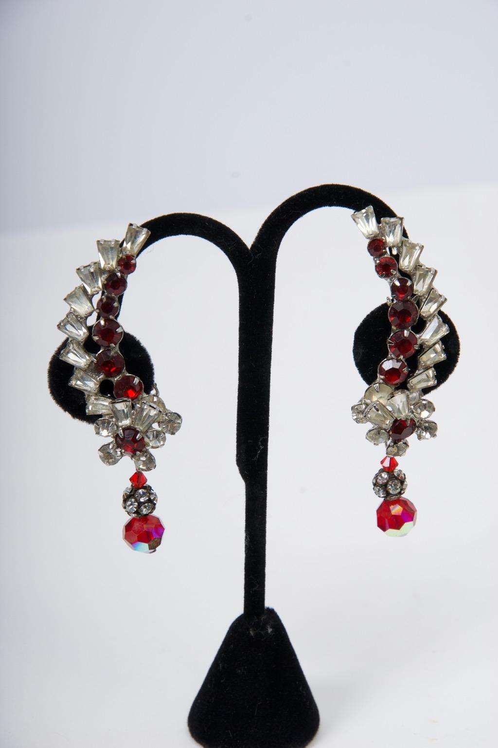 Dramatic rhinestone and ruby stone ear clips that follow the curve of the earlobe. The earpiece, composed of clear and ruby crystals, tapers at the top and terminates in an applied floral motif that suspends a rhinestone rondel and faceted red