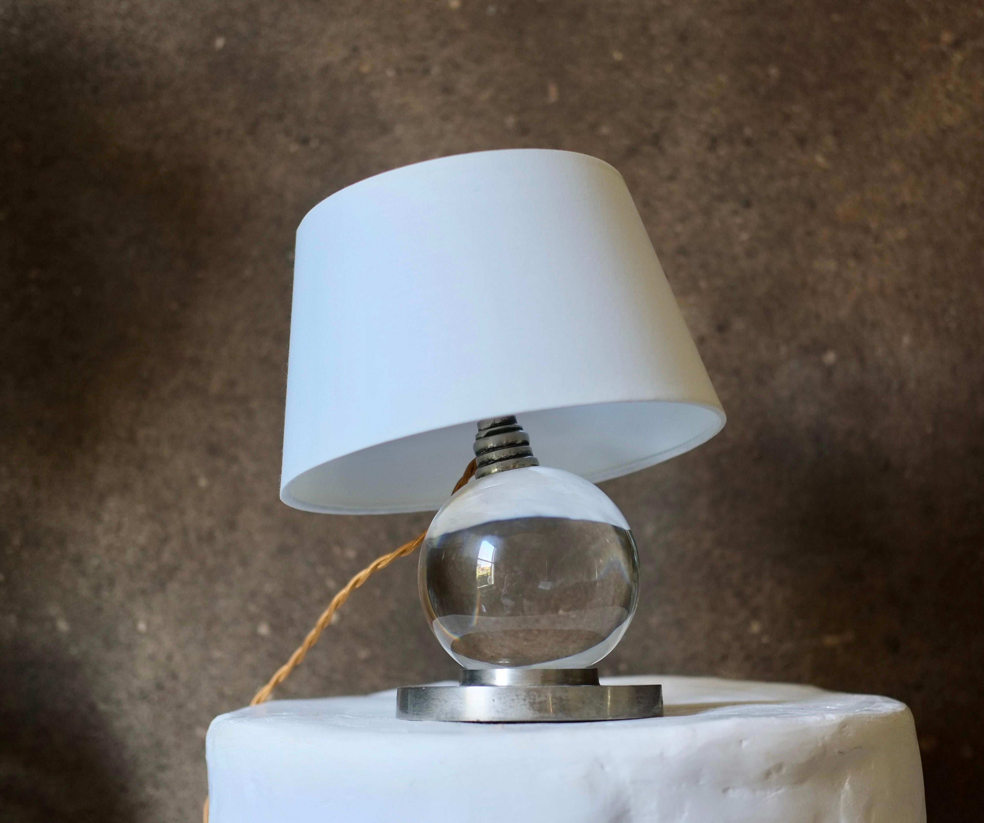 A crystal glass ball lamp mounted on a metal base attributed to Jacques Adnet.

Rewired and fitted with a UK plug. 

Dimensions including shade H 24 Dia 20 cm