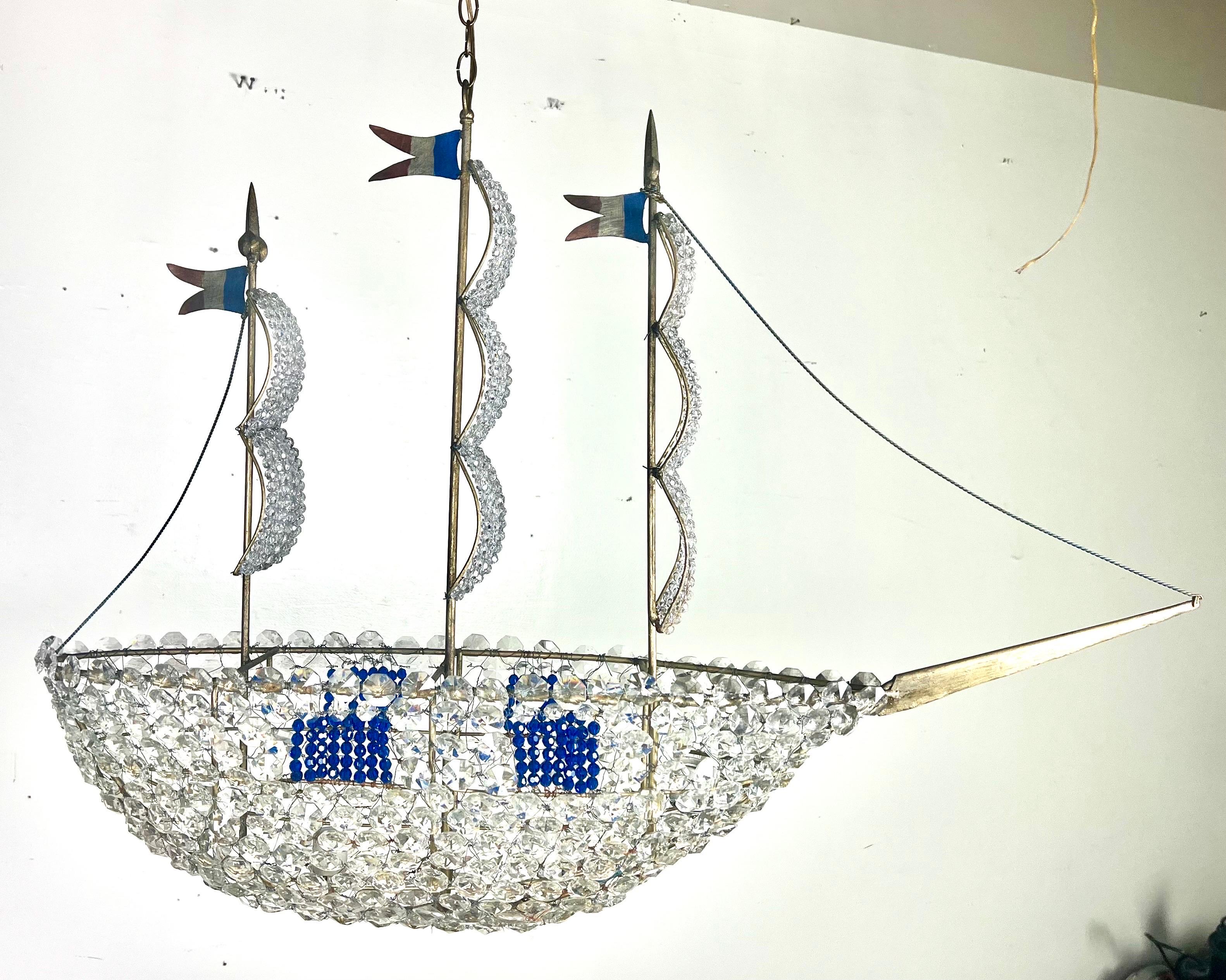 A custom, one-of-a-kind hand beaded ship featuring blue bead accents, metal flags, crystals, and larger crystals at the base, with smaller beads on the sails.  This monumental piece is truly unique and would add a fabulous and distinctive touch to