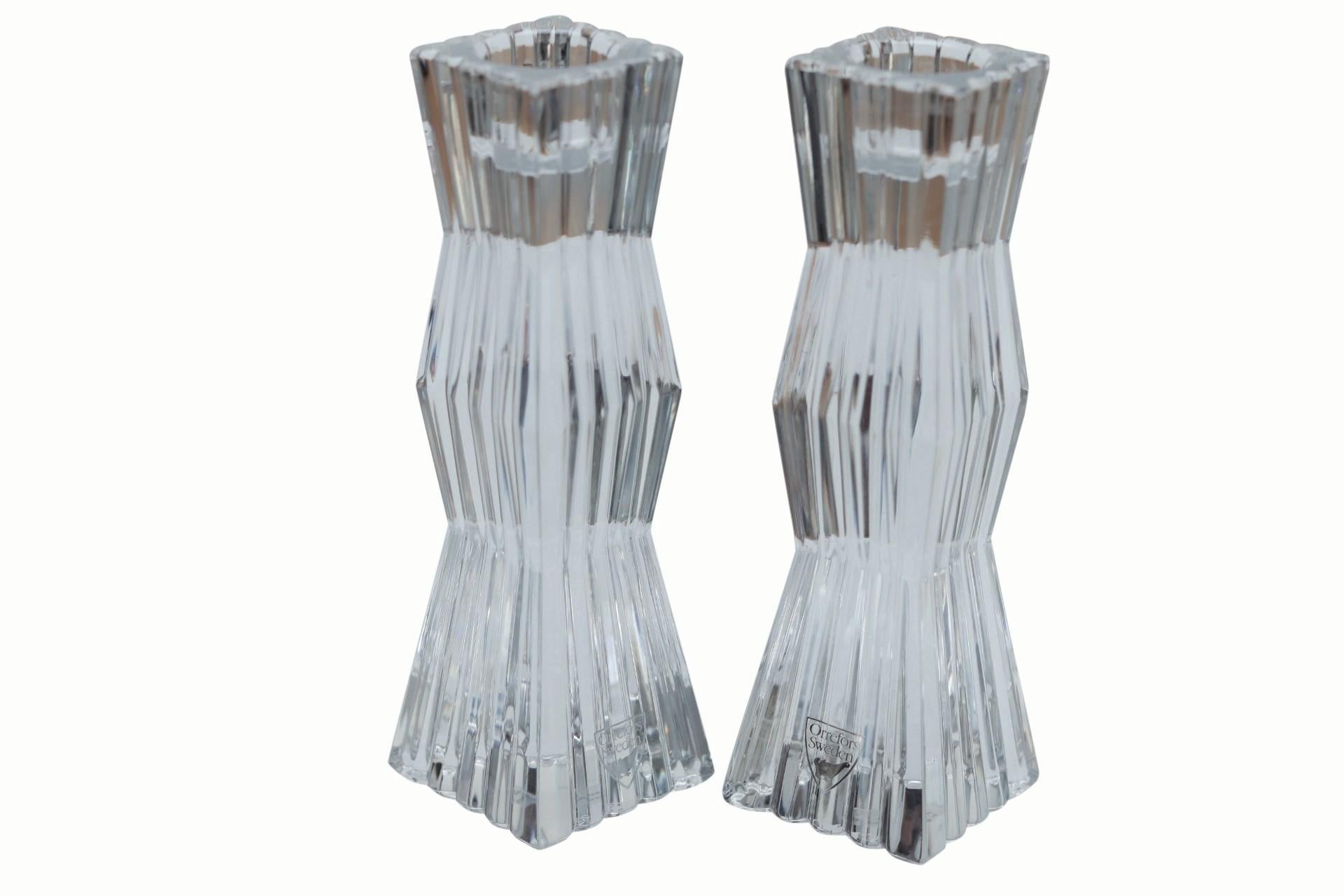 A pair of crystal candlestick holders made by Orrefors of Norway. Angular squared columns are reeded with scalloped tops and marked underneath ‘Made in Austria’. Dimensions per candlestick.