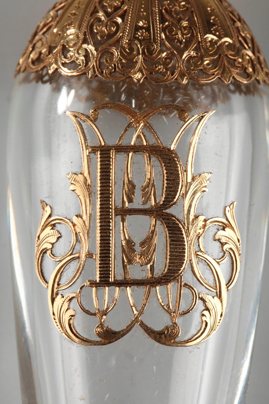 eardrop-shaped crystal flask in pierced gold mount, intricately sculpted with hearts, palmettes, and scrollwork. The mounting is set on the base and the neck, and a large letter B is highlighted on the paunch of the flask. The delicately sculpted,