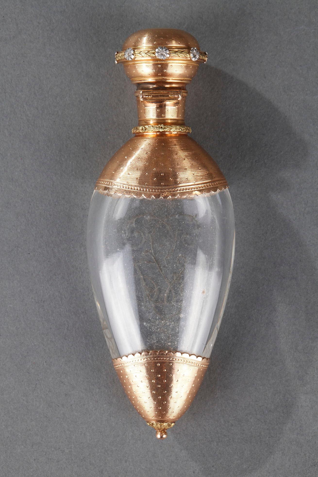 Peardrop-shaped crystal flask in gold mount. The body is finely engraved with an interlaced monogram. The mounting is decorated with an intricate engraved parallel stripes and dots. The cork and the collar are decorated with a floral frieze in