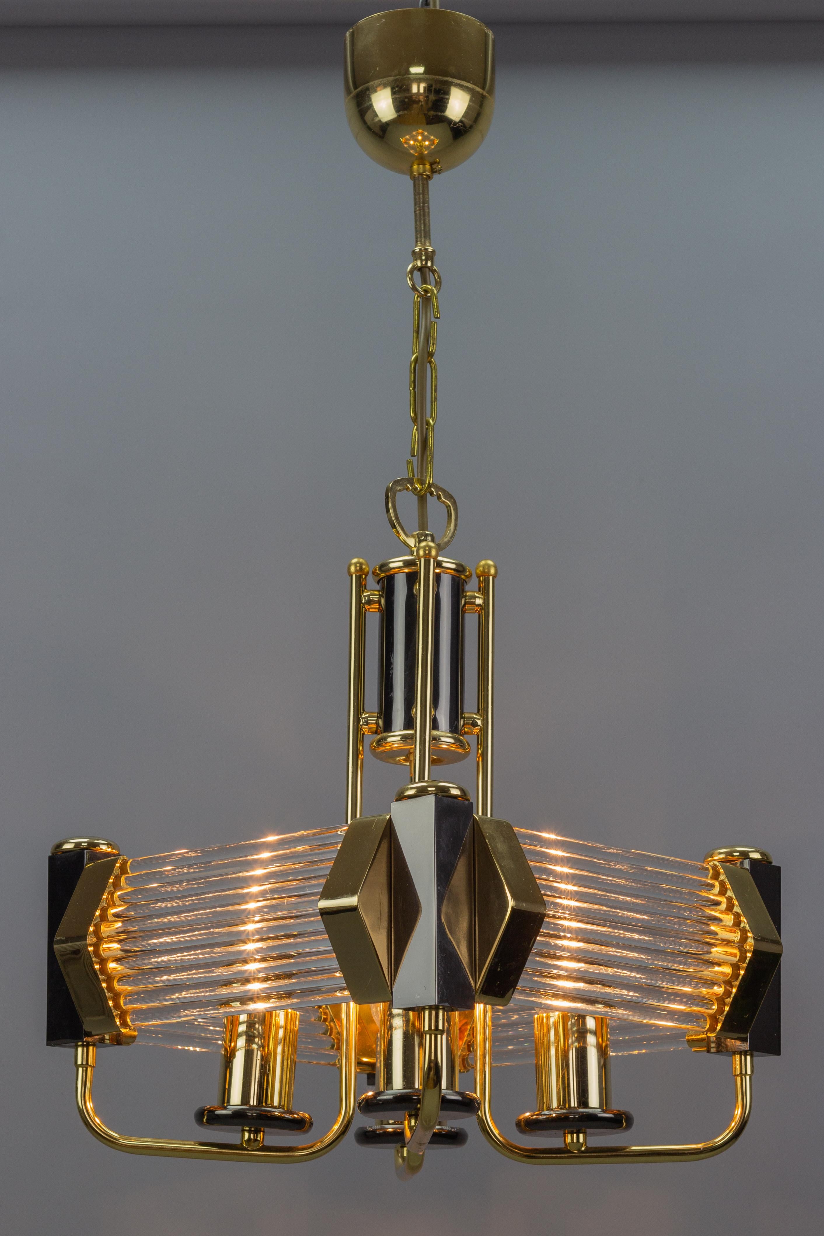 Elegant Hollywood Regency-style chandelier from the 1970s - 1980s. This beautiful four-light hanging chandelier features a gold-plated brass frame with black lacquered brass parts and clear crystal glass rods/tubes, a brass chain, and a canopy.
Four