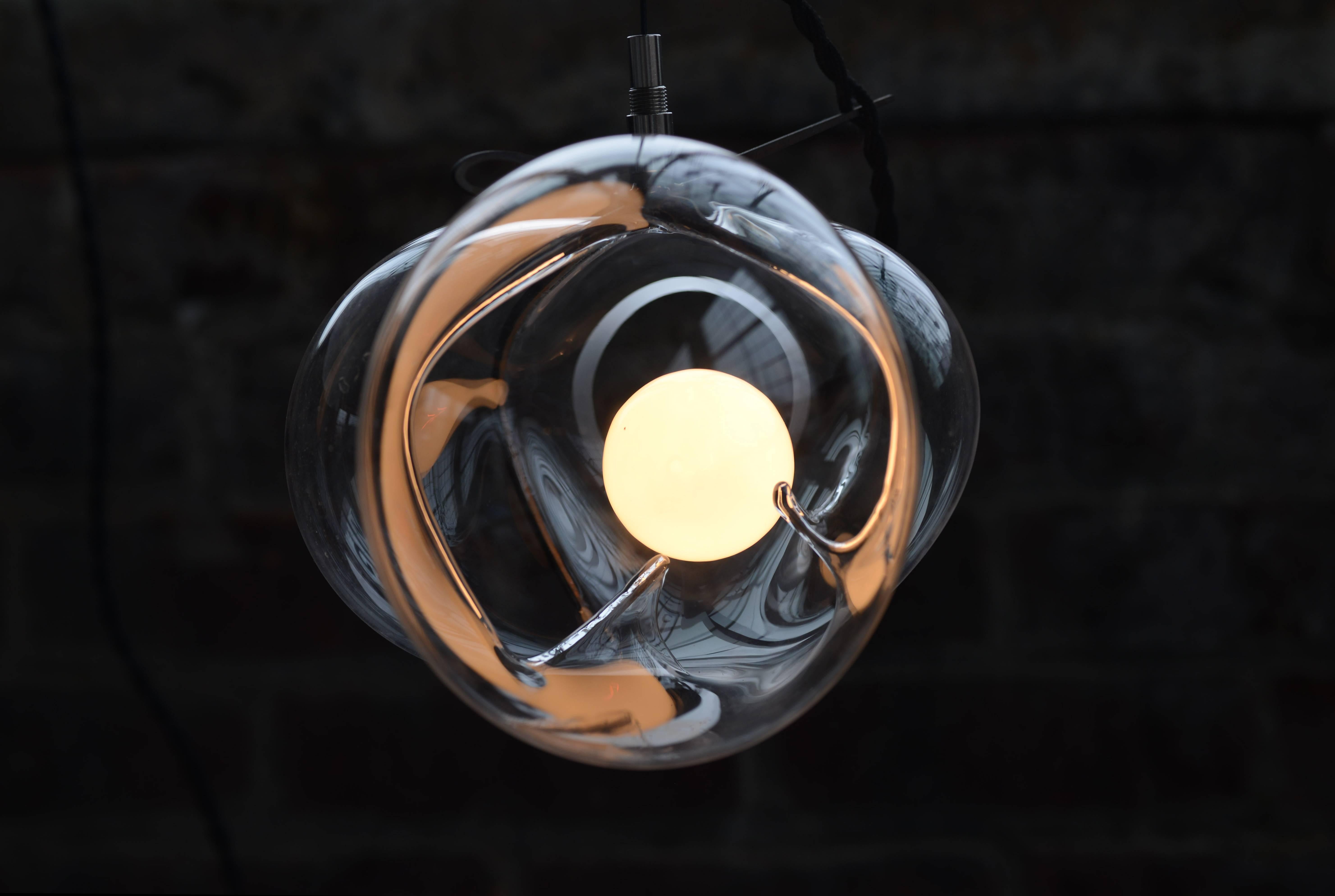 Aufhängung aus Kristallglas, exhale von Catie Newell, WDSTCK Studio
Maße: Durchmesser 30 cm
MATERIALIEN: Kristallglas, rostfreier Stahl.

Exhale umhüllt gekonnt einen einzelnen Glasblasen in
eine starre Metallstruktur. Die Metallform schränkt