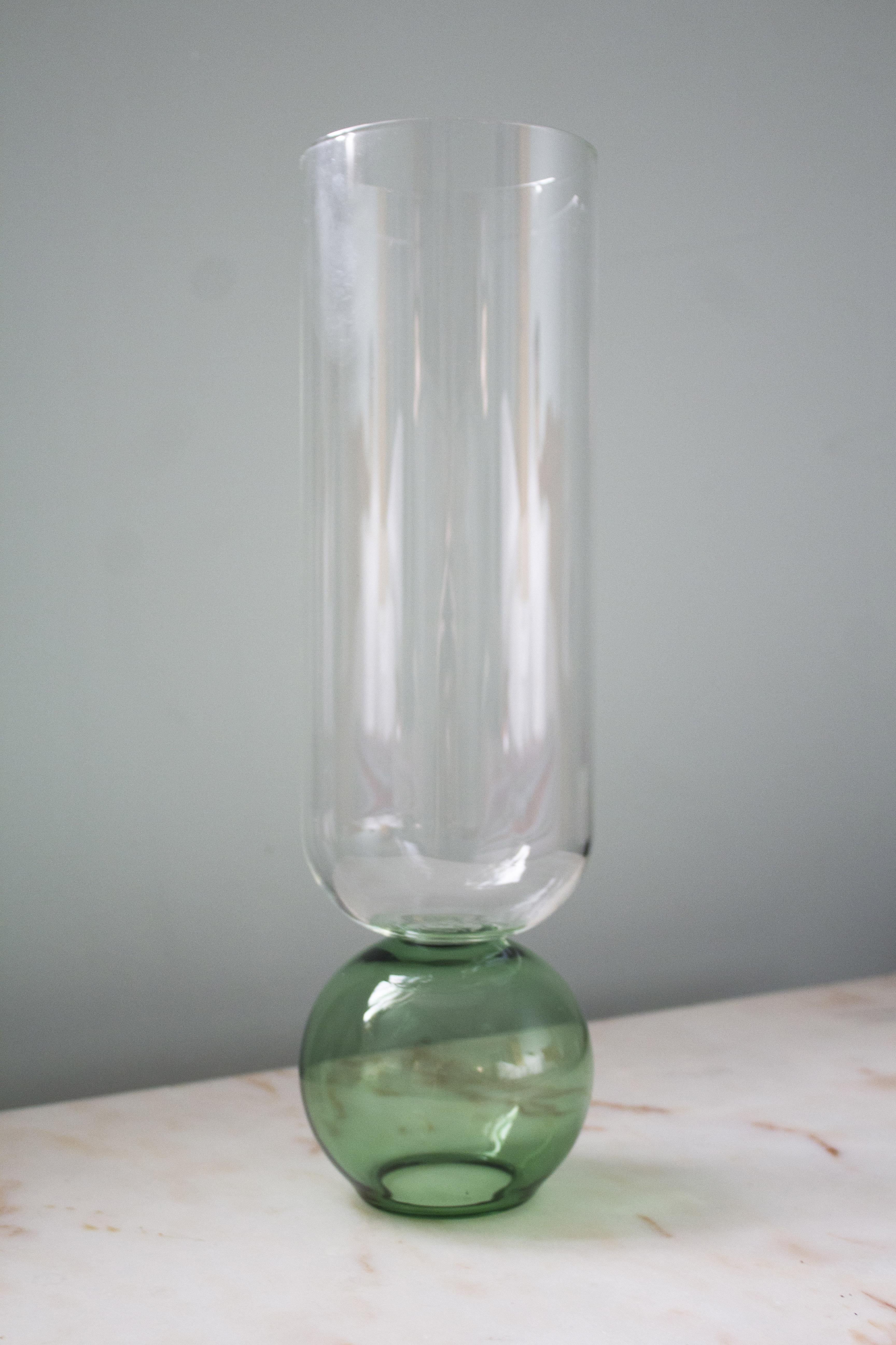 Ce charmant vase fabriqué à la main en verre fin est un écrin de volumes purs. Sa silhouette élégante est composée d'une base sphérique verte soutenant le corps cylindrique transparent. Fabriqué selon les techniques traditionnelles du XIXe siècle,