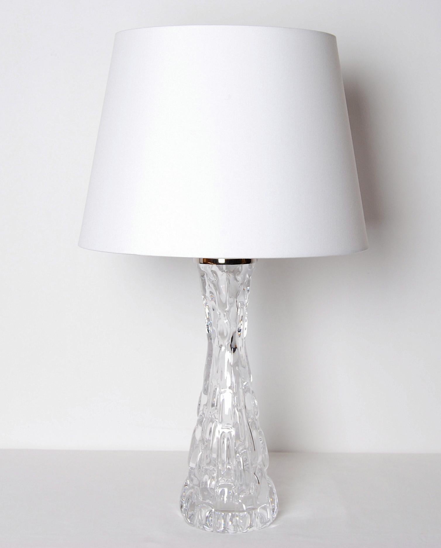 The smaller version of model RD 1477 table lamp in crystal glass by Carl Fagerlund for Orrefors, Sweden. The heavy hour glass form base is made of crystal glass. Polished nickel plated fittings.
Signed in bottom. Please note: We are selling this
