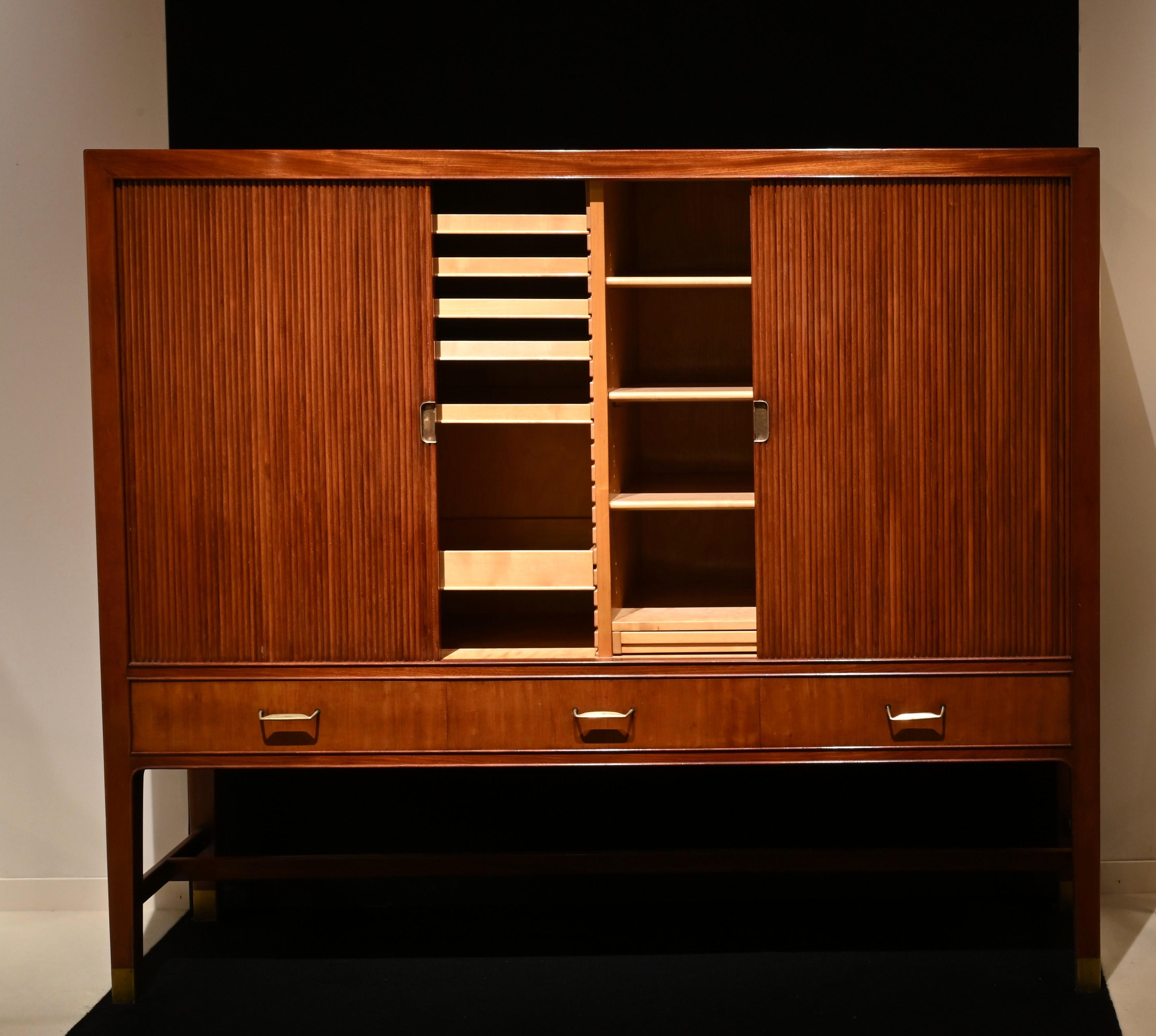 Un raro ed elegante mobile in mogano cubano con piedini e maniglie in ottone, opera del designer americano William Watting che visse e lavorò in Danimarca negli anni Cinquanta e Sessanta. Si apre con 2 ante a tamburo che si inseriscono lateralmente