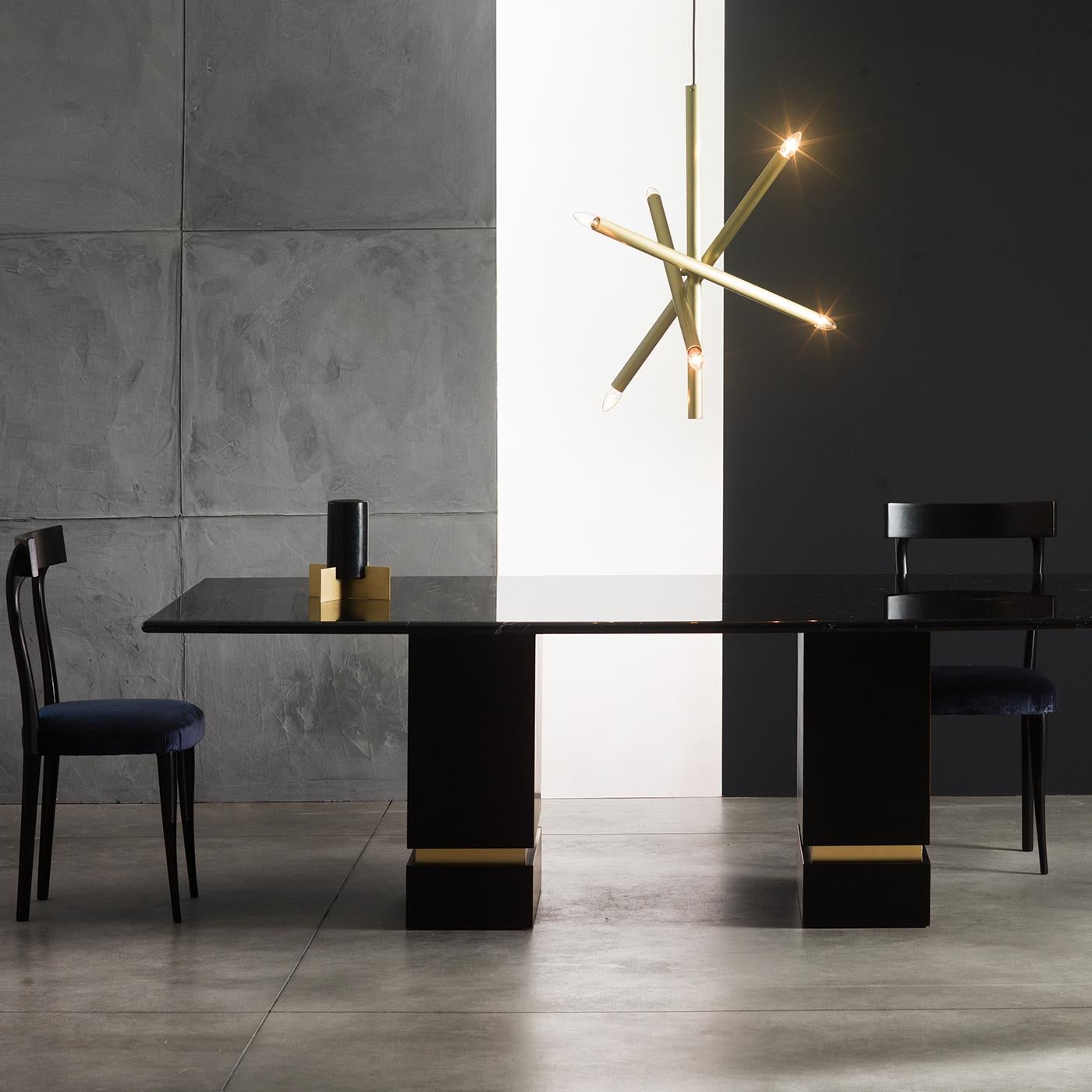 This statement dining table exudes a minimalist elegance, defined by understated geometric lines. Its Marquina black marble top rests upon two wooden cube-shaped bases, embellished with brushed brass inserts. Thanks to its sleek silhouette and