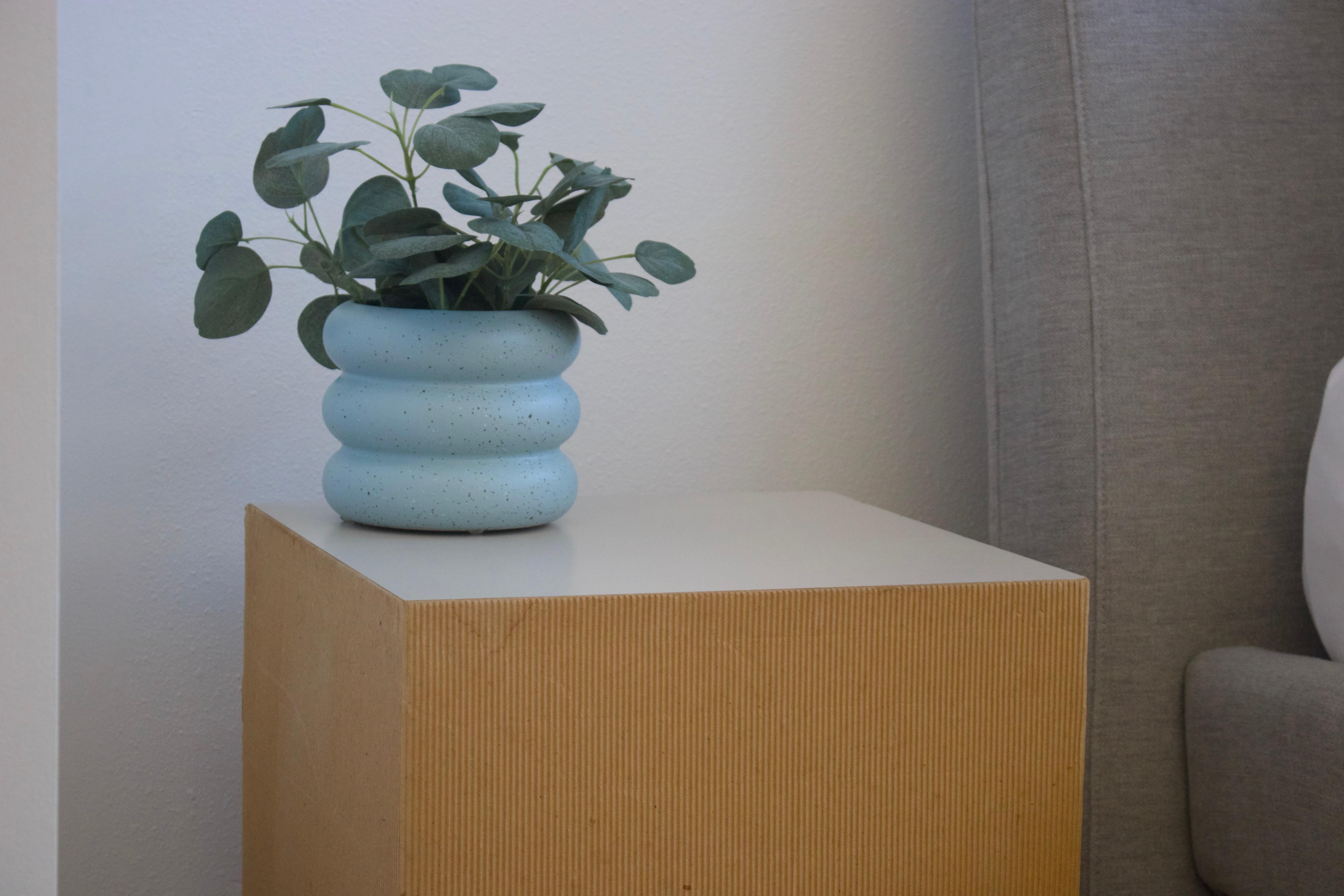 A cubed, corrugated cardboard end table/pedestal with laminated top finish, measuring 15.75” cubed.