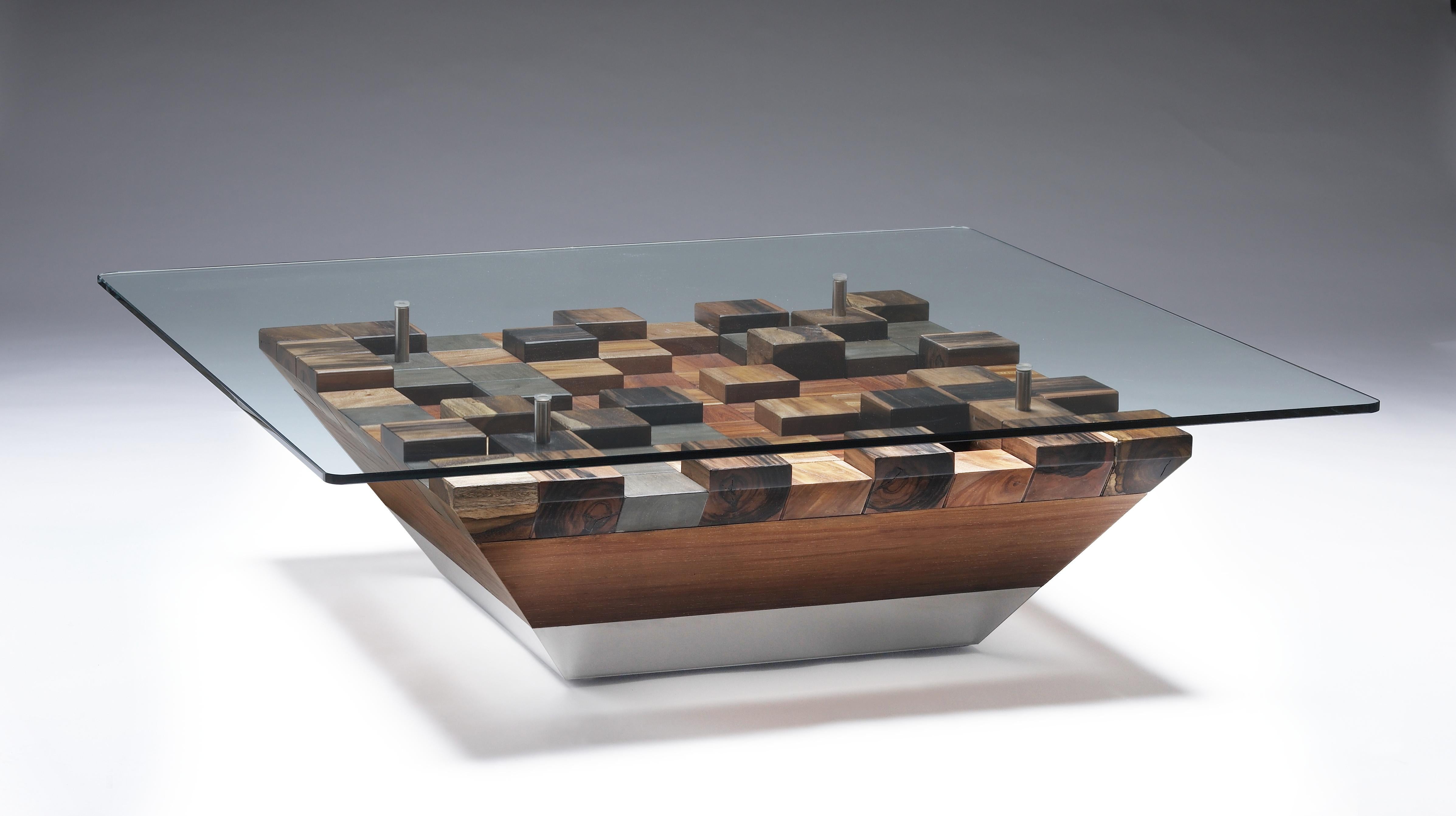 The base of this glass-top table is crafted from an intriguing combination of woods and stainless steel, forming captivating geometric shapes. This unconventional design adds a distinctiveness to the piece, making it truly remarkable. The use of