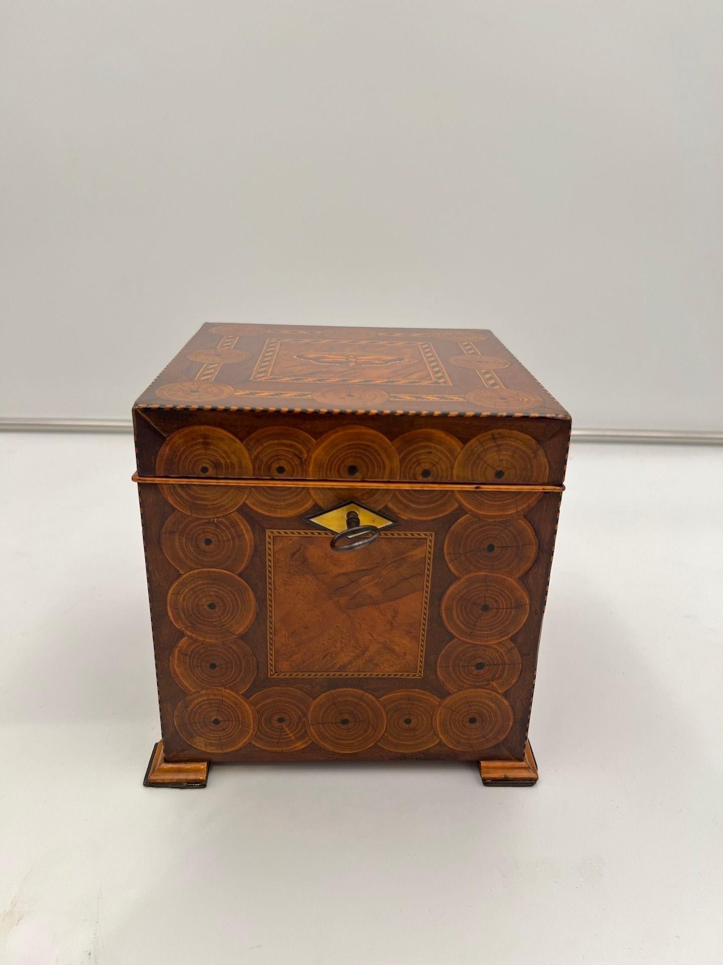 Cube-shaped, elaborately crafted Biedermeier casket. Walnut veneered.
Inlay work with branch slices and mahogany veneer. Several band inlays in maple and ebony.
Top center with inlaid butterfly in maple with fire burnt decor. Interior covered with