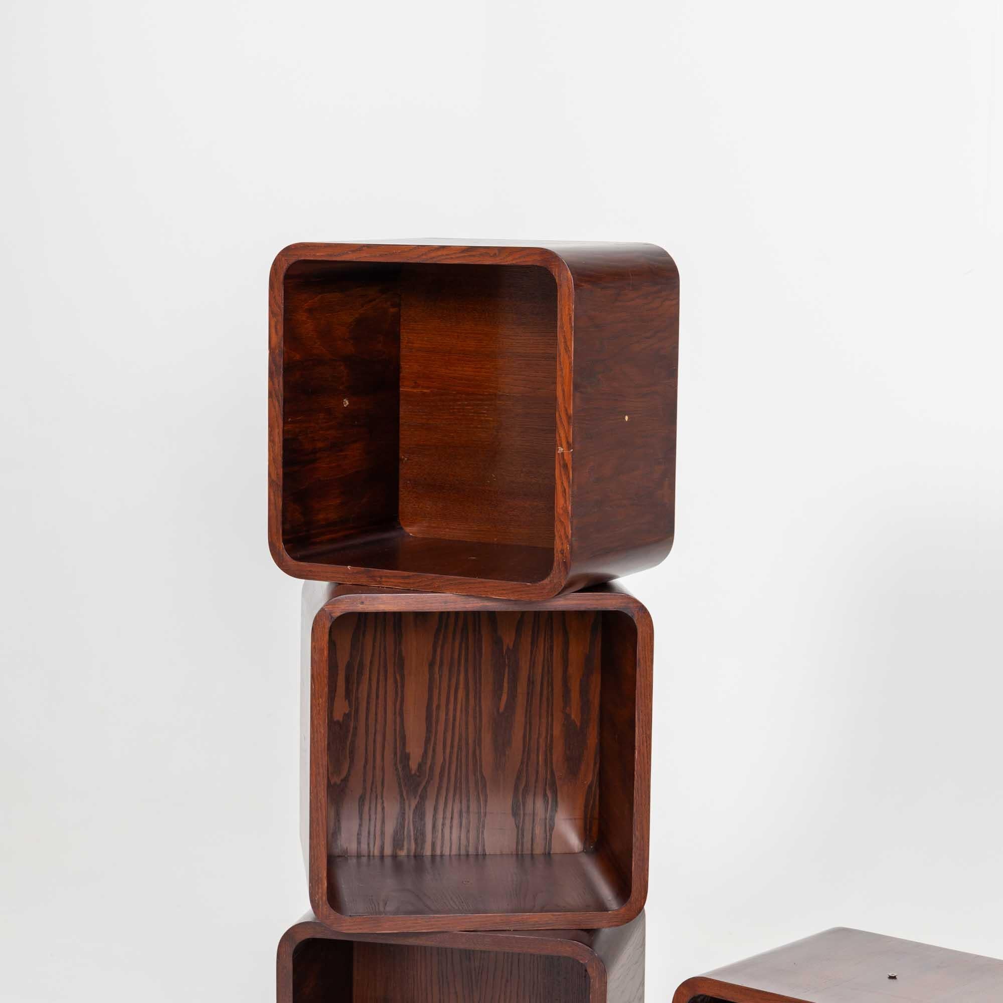 Set of four cube-shaped shelf elements that can be combined as desired. The elements are stained dark brown and are connected to each other by means of screws.