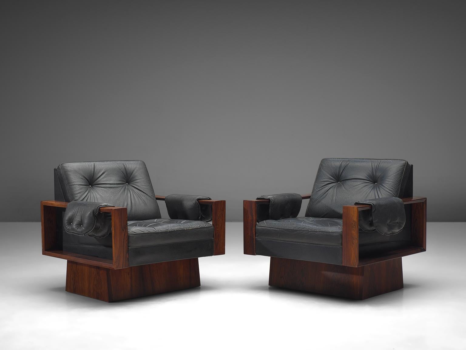 Easy chairs, black leather and rosewood, Europe, 1970s.

This set of lounge chair features a rosewood frame with open armrest back and an angular, geometric frame. A wonderful detail in this set are the pillows that flow over the strict angular