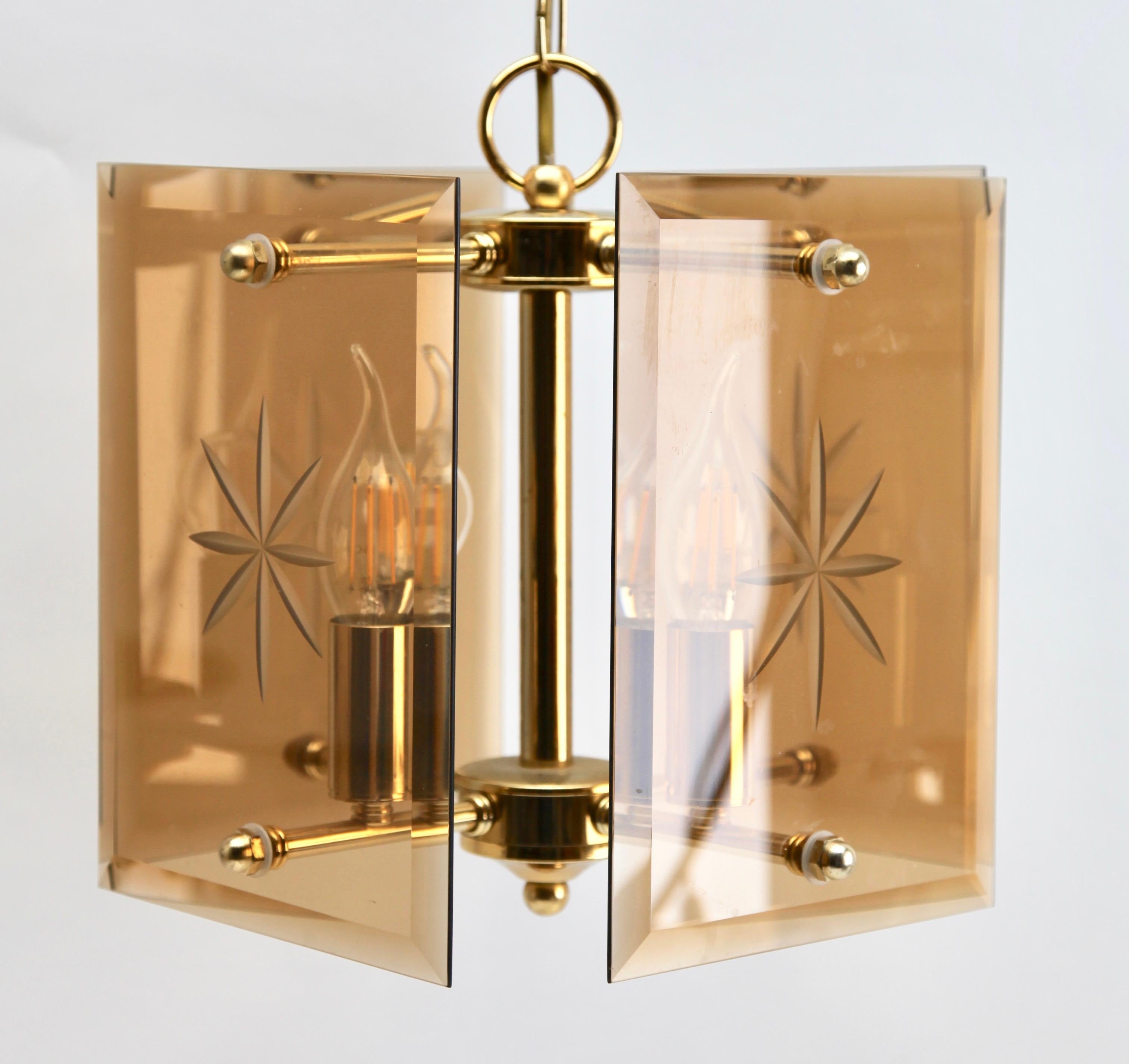 Geometric modernist design on a brass-patinated stem. Central chain and column with four pairs of arms supporting four lamps in candlestick form, and four bronze colored glass sheets acting as shades, each with an engraved star motif.
This simple