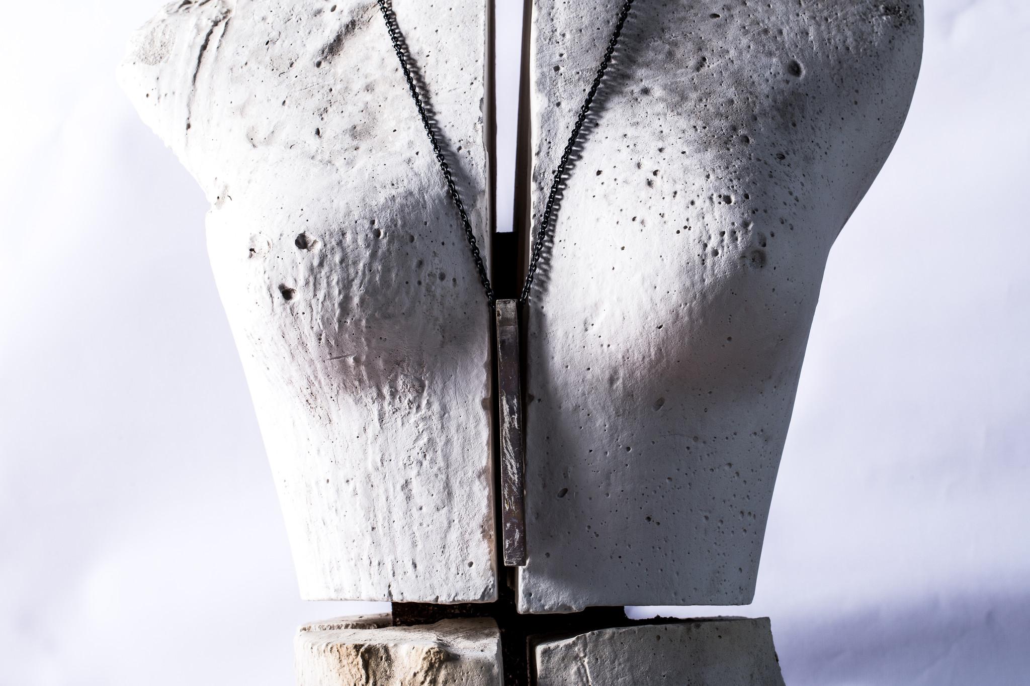 Collier pendentif en forme de parallélépipède en laiton, monté sur une chaîne de 74 cm en argent sterling oxydé. Le substrat en laiton est plaqué par électrolyse avec de l'or 18k, puis plongé dans un bain d'acide lourd. Une fois la détérioration