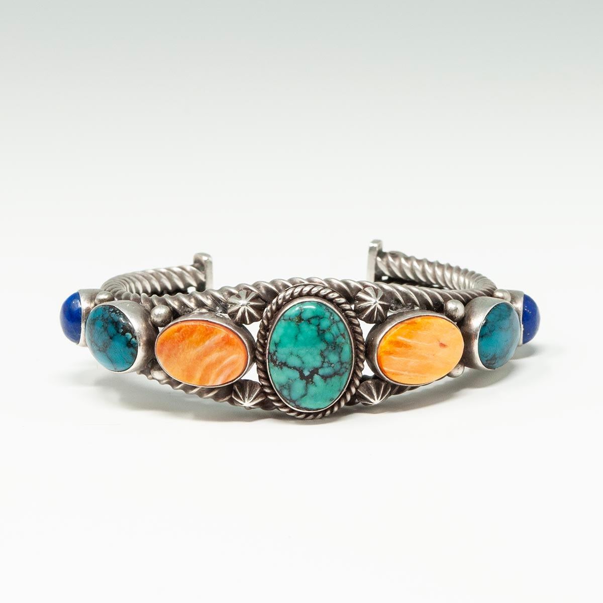Pulsera brazalete del artista navajo Aaron Toadlena

Esta hermosa pulsera brazalete fue hecha a mano por el renombrado orfebre navajo Aaron Toadlena. La cuerda de plata retorcida ancla siete cabujones de turquesa, lapislázuli y concha de ostra