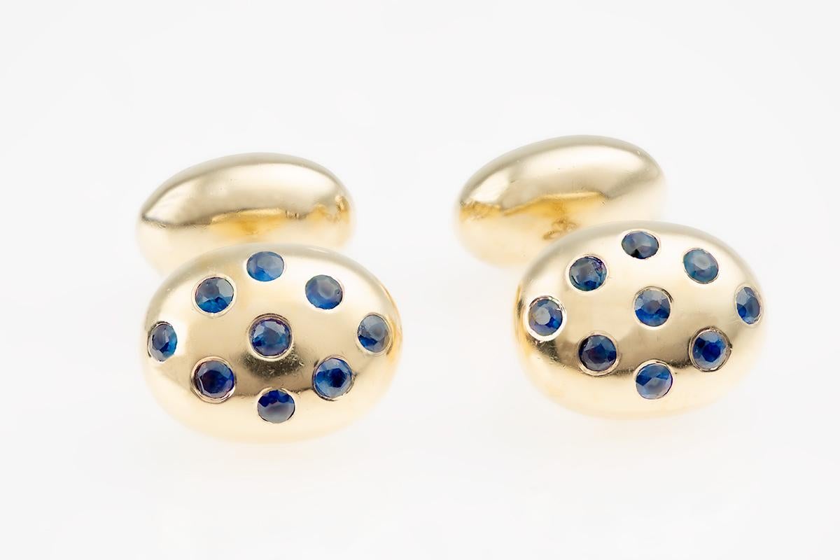 1970’s vintage double sided cufflinks in 18 karat yellow gold. Shaped in the design of a coffee bean in two sizes with chain link connections. The smaller bean set with one single sapphire and the larger bean set with nine sapphires. Hallmarked with