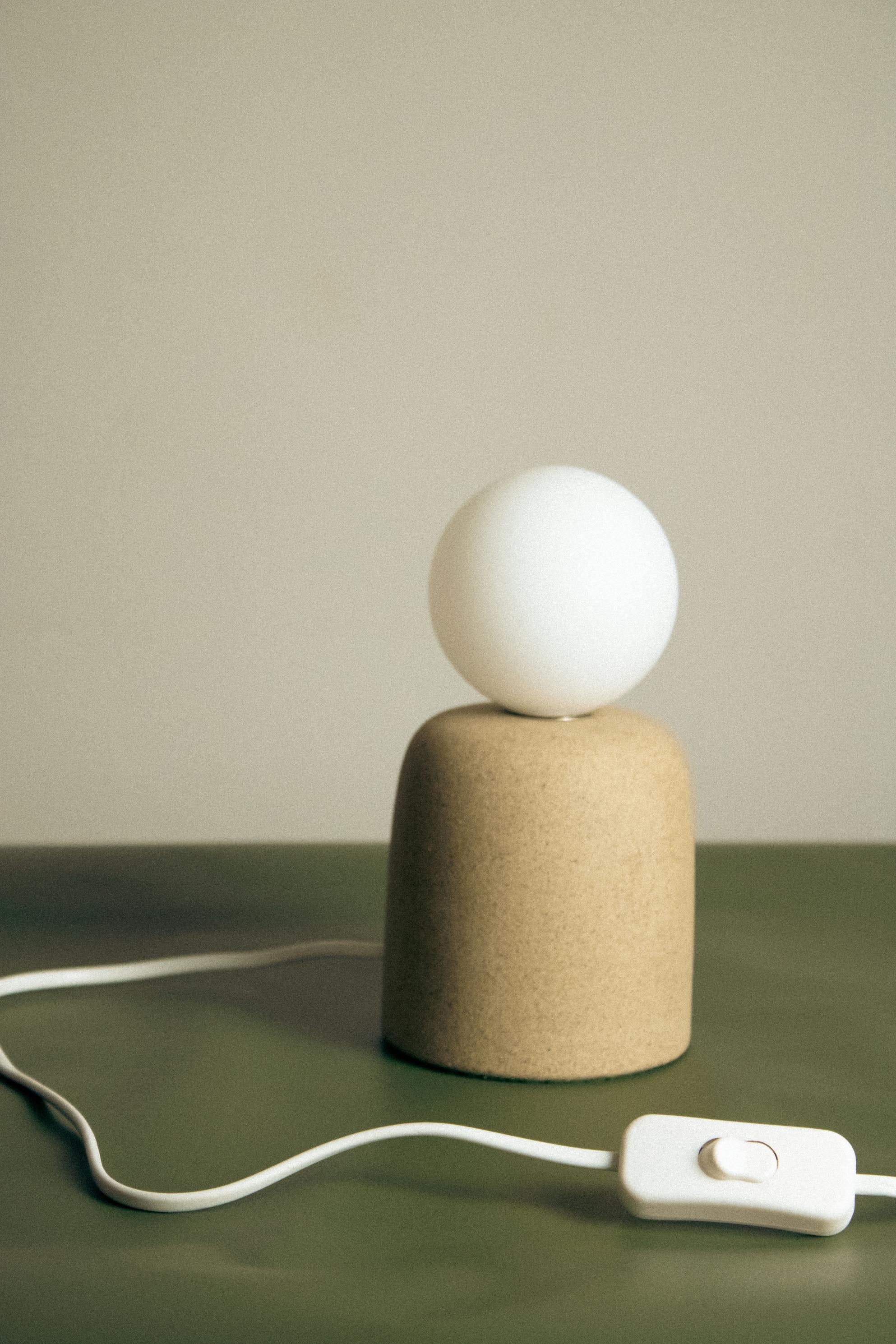 La lampe à poser Cuia fait partie de la collection Romaria, elle a été développée par Raísa Anderson, créatrice de la marque, et produite à l'intérieur de São Paulo, à partir d'argile, des mains de Luis Airton, céramiste partenaire avec plus de 30