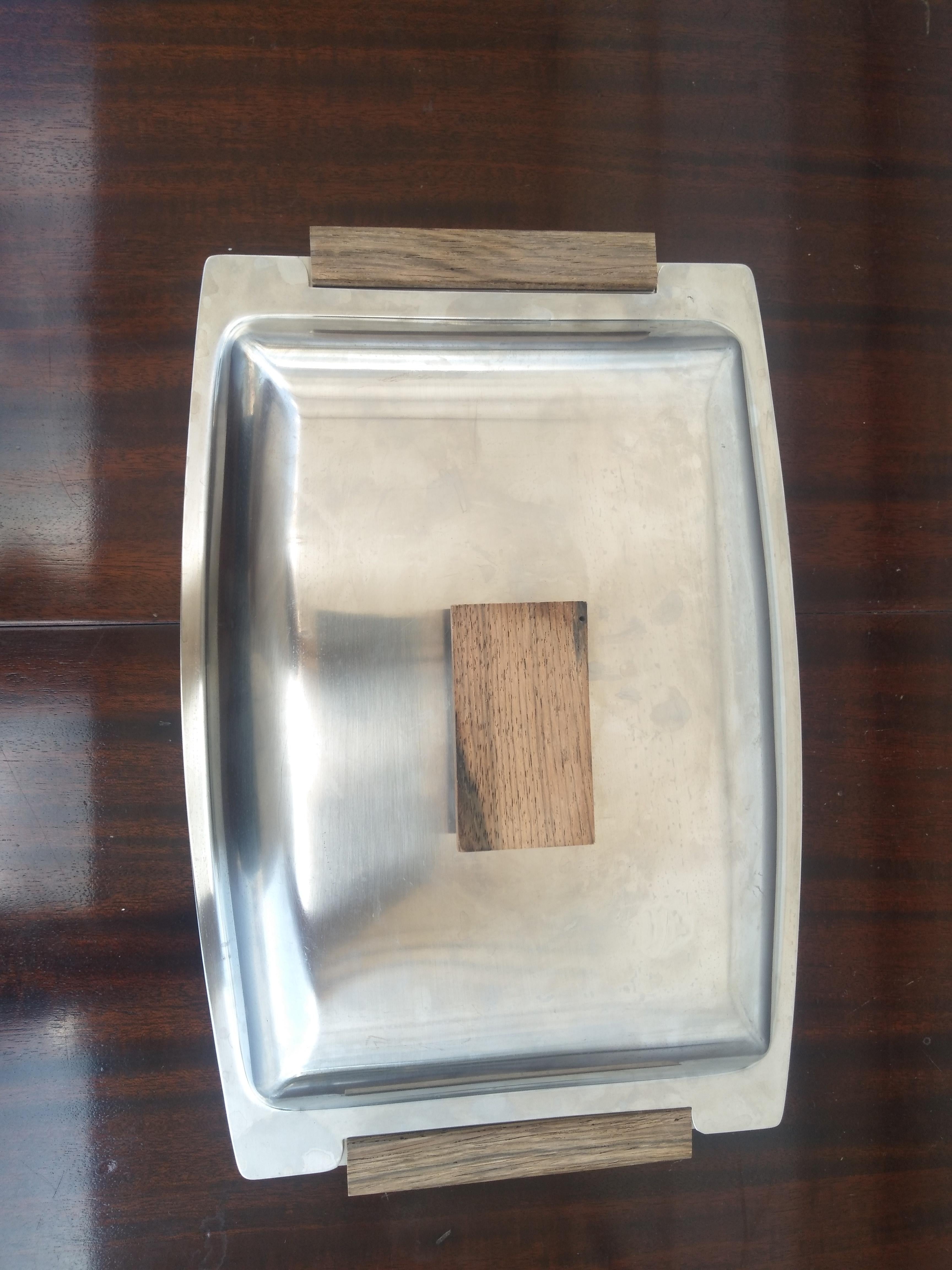 Fabricada en Italia por Cultural, esta fuente con tapa tiene asas laterales y de la tapa de madera de teca. Está hecha de acero inoxidable y es una pieza de vajilla impresionante.