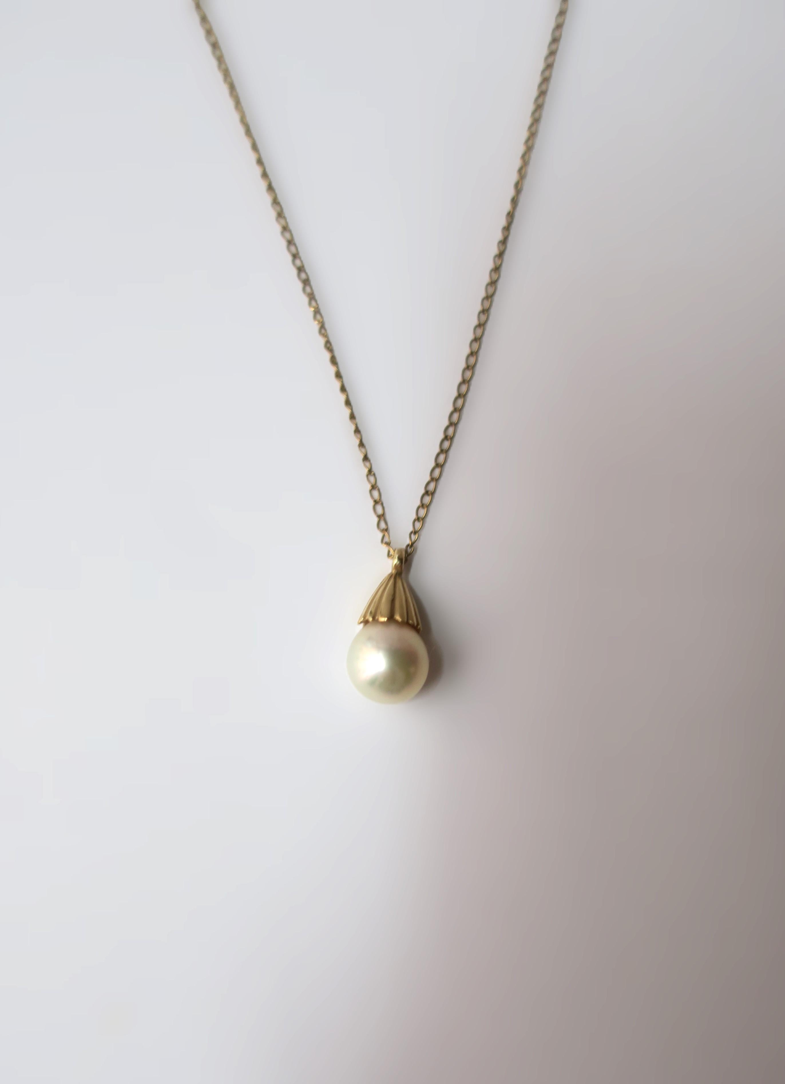 A very beautiful white cultured pearl on a 14-karat yellow gold necklace, circa mid-20th century. Pearl is very beautiful with a high luster. Pearl has a 14-karat yellow gold crown-like design at top attached to 14-karat yellow gold necklace. A