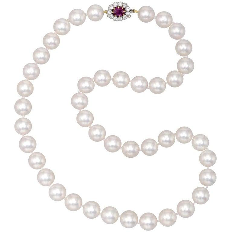 Cultured pearl necklace, composed of 43 graduated cultured pearls with diameters ranging from 10mm to 9.5mm, strung on a hand-knotted silk cord, with an antique oval-shaped clasp in 18k yellow gold and platinum set with an oval-shaped ruby weighing