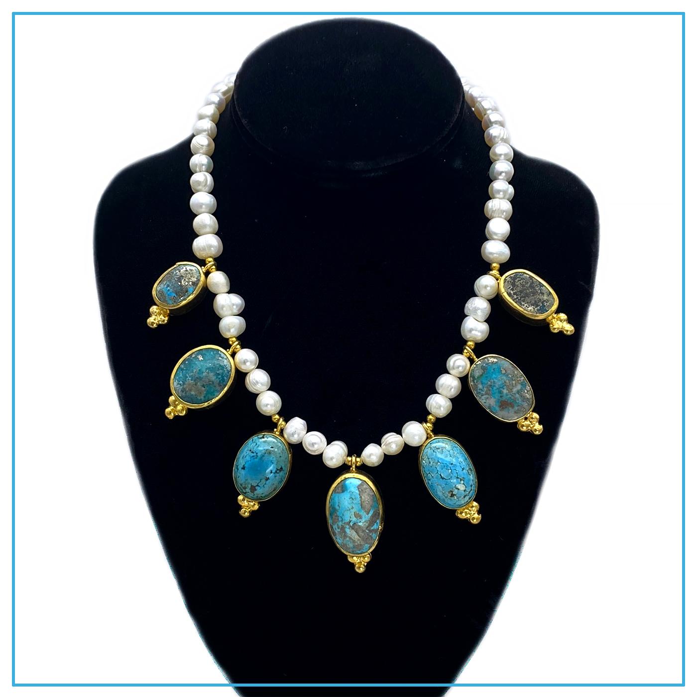 Si tratta di una collana di perle coltivate incastrate a mano con sette ciondoli di turchese che pendono sul davanti. Viene dalla Turchia. Queste grandi pietre di turchese levigato sono avvolte in metallo dorato decorato. La collana si collega con