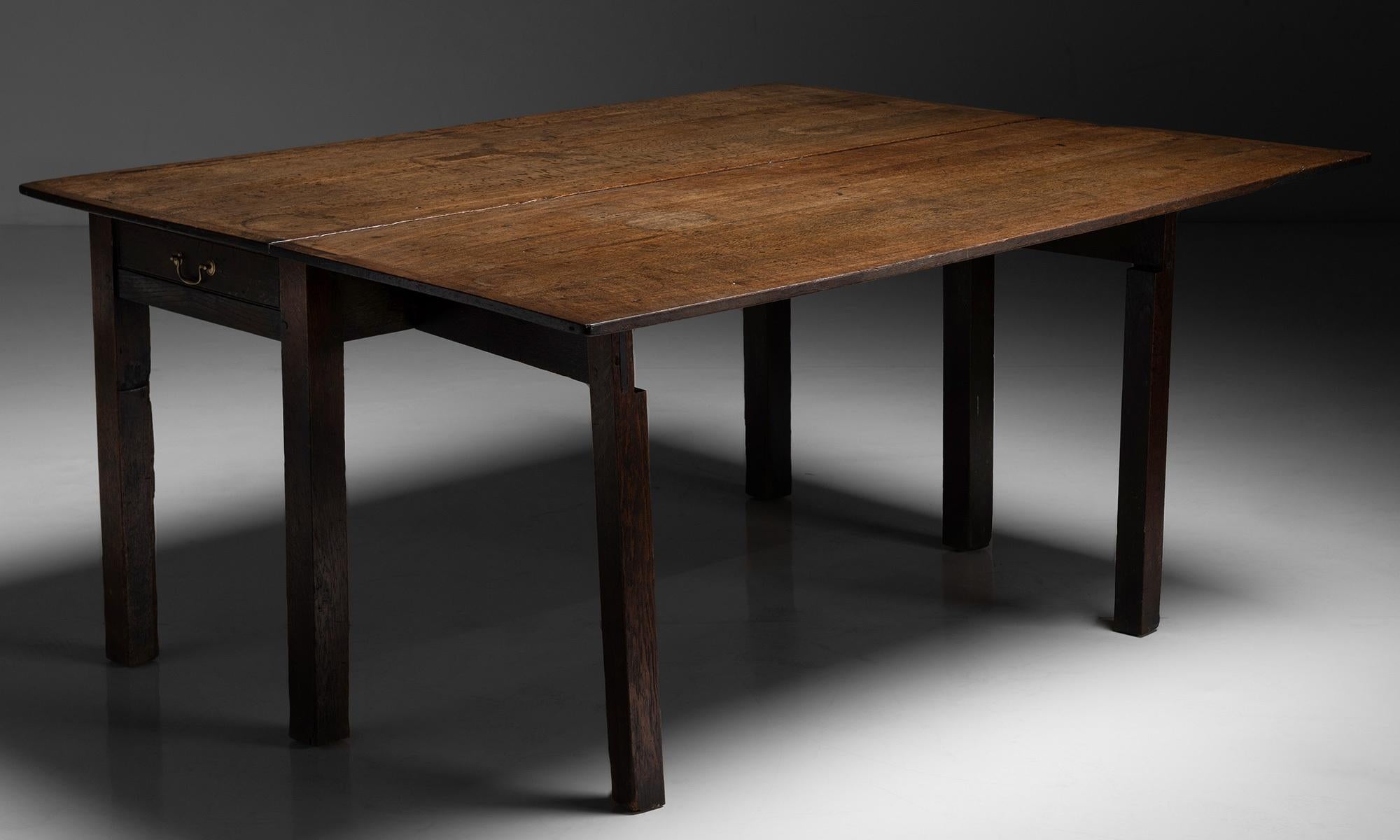 Cumbrian oak dining table.

England, circa 1789.

Unique dining table with a leaf to one side. Designed to be sat at along one side with the drop leaf against the wall, and then pulled out to seat additional guests.

Measures: 64.25” L x