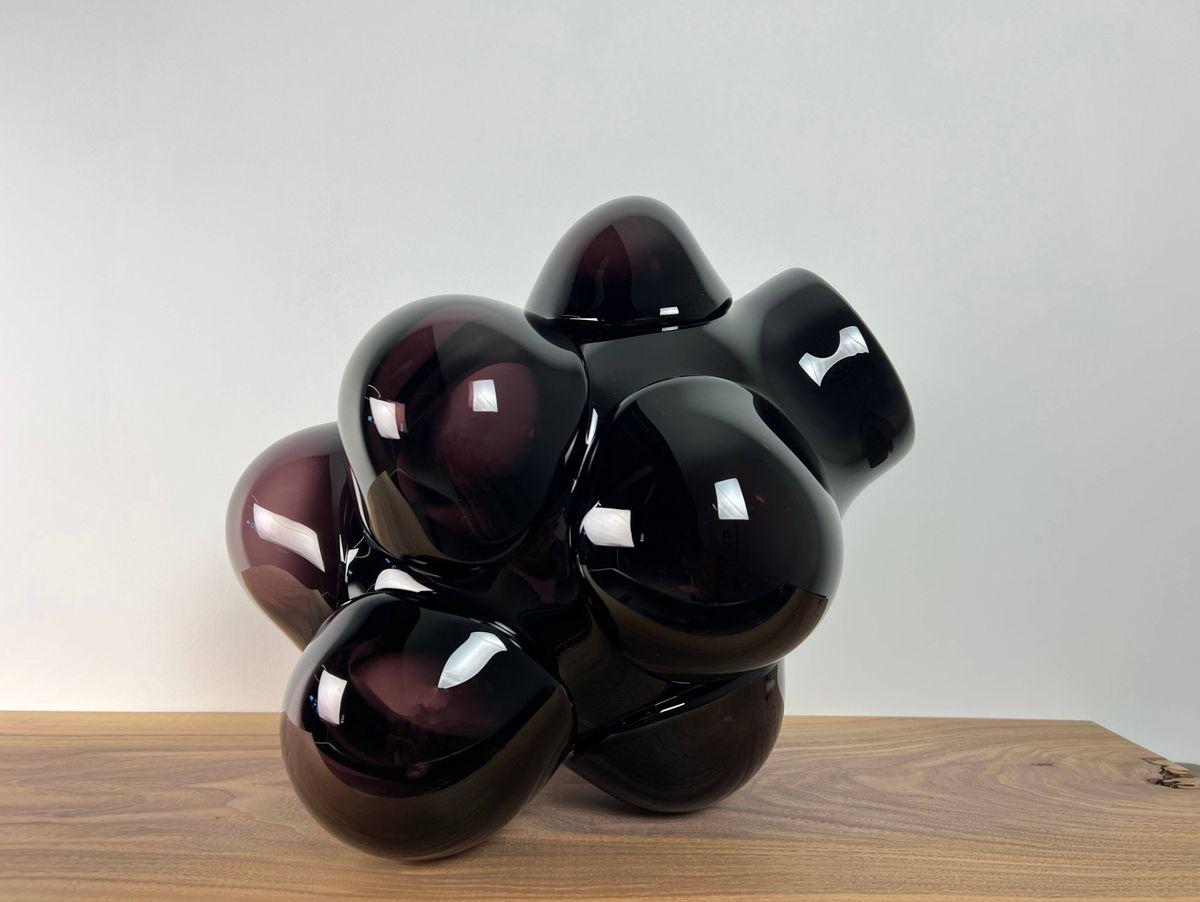 These pieces use dollops of glass over a central core. The hot bits are blown out to diffuse the color and create a bulbous cloud-like shape. The bulbs are arranged so that each vase will sit in a way unique to itself. Hand blown and shaped in lead