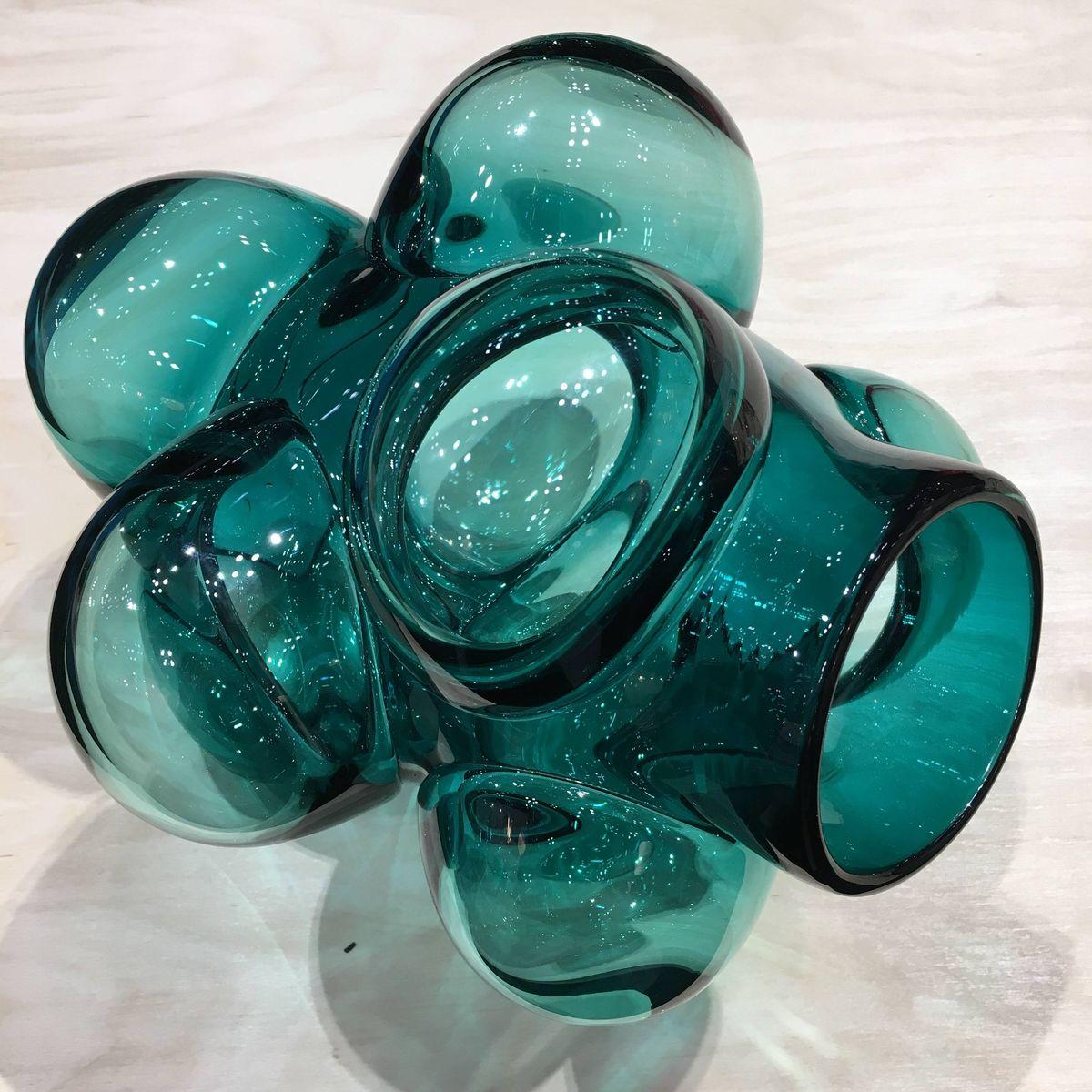 These pieces use dollops of glass over a central core. The hot bits are blown out to diffuse the color and create a bulbous cloud-like shape. The bulbs are arranged so that each vase will sit in a way unique to itself. Hand blown and shaped in lead