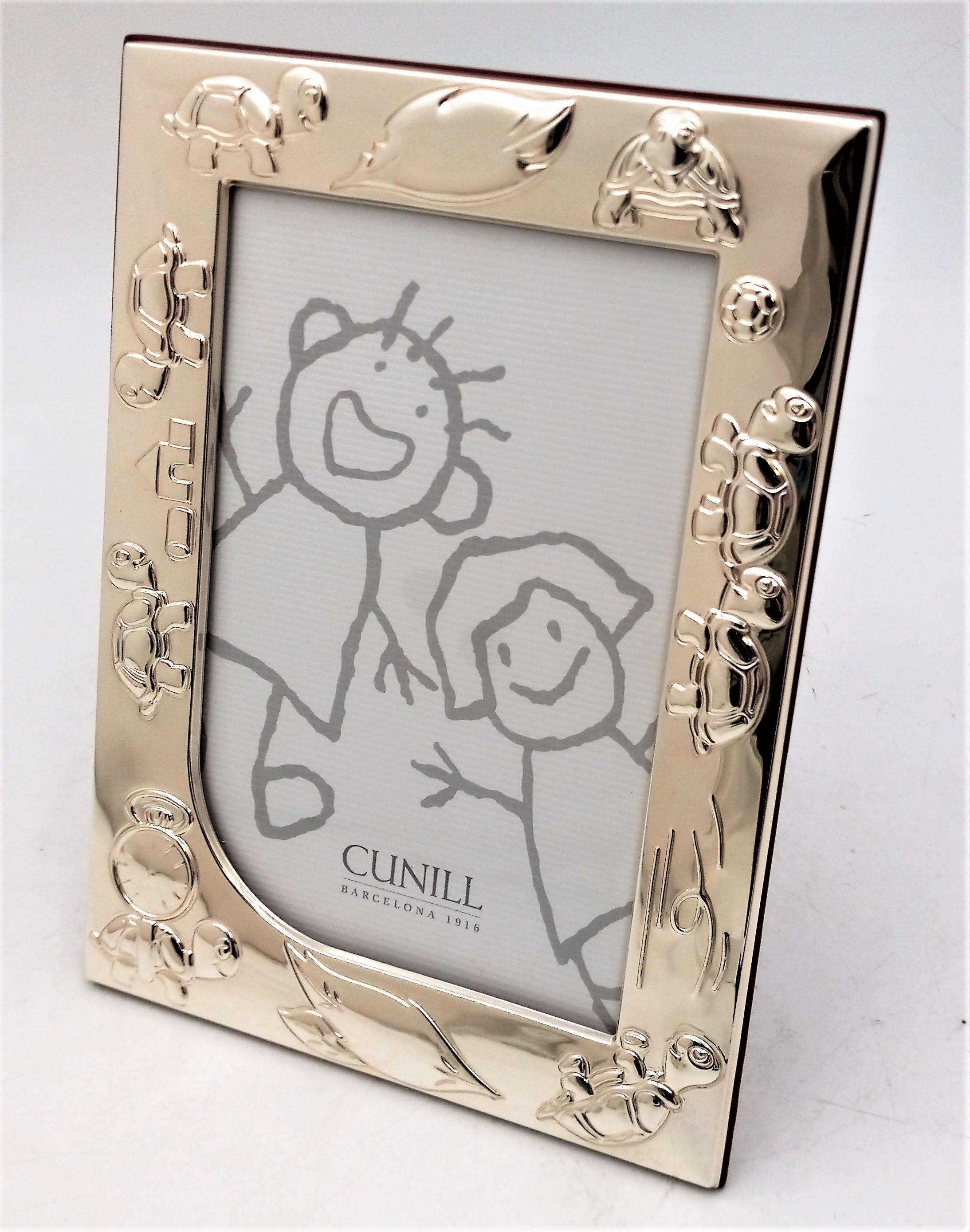 A sterling silver picture frame by Cunill. Burgandy-painted wood easel backing and a silver clasp to secure that the backing is closed. As seen, the front of the frame is decorated by frolicking turtles in a full border. Measures 5 3/4 inches wide