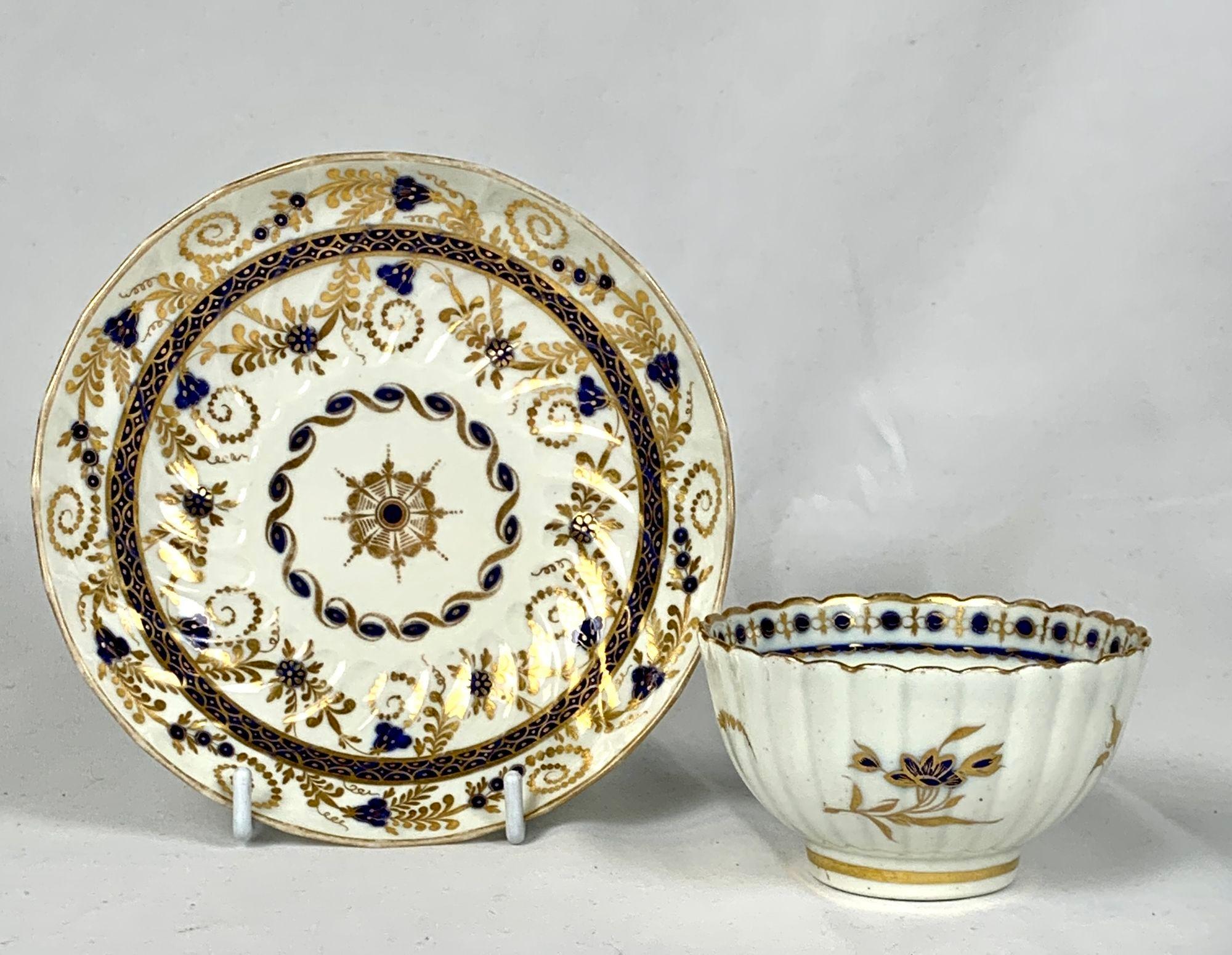 This lovely 18th-century porcelain tea bowl and saucer were made by Caughley Porcelain in England circa 1785.
The style is neoclassical: both the cup and saucer show a gilded star at the center and rings of decoration, combining deep blue enamel and