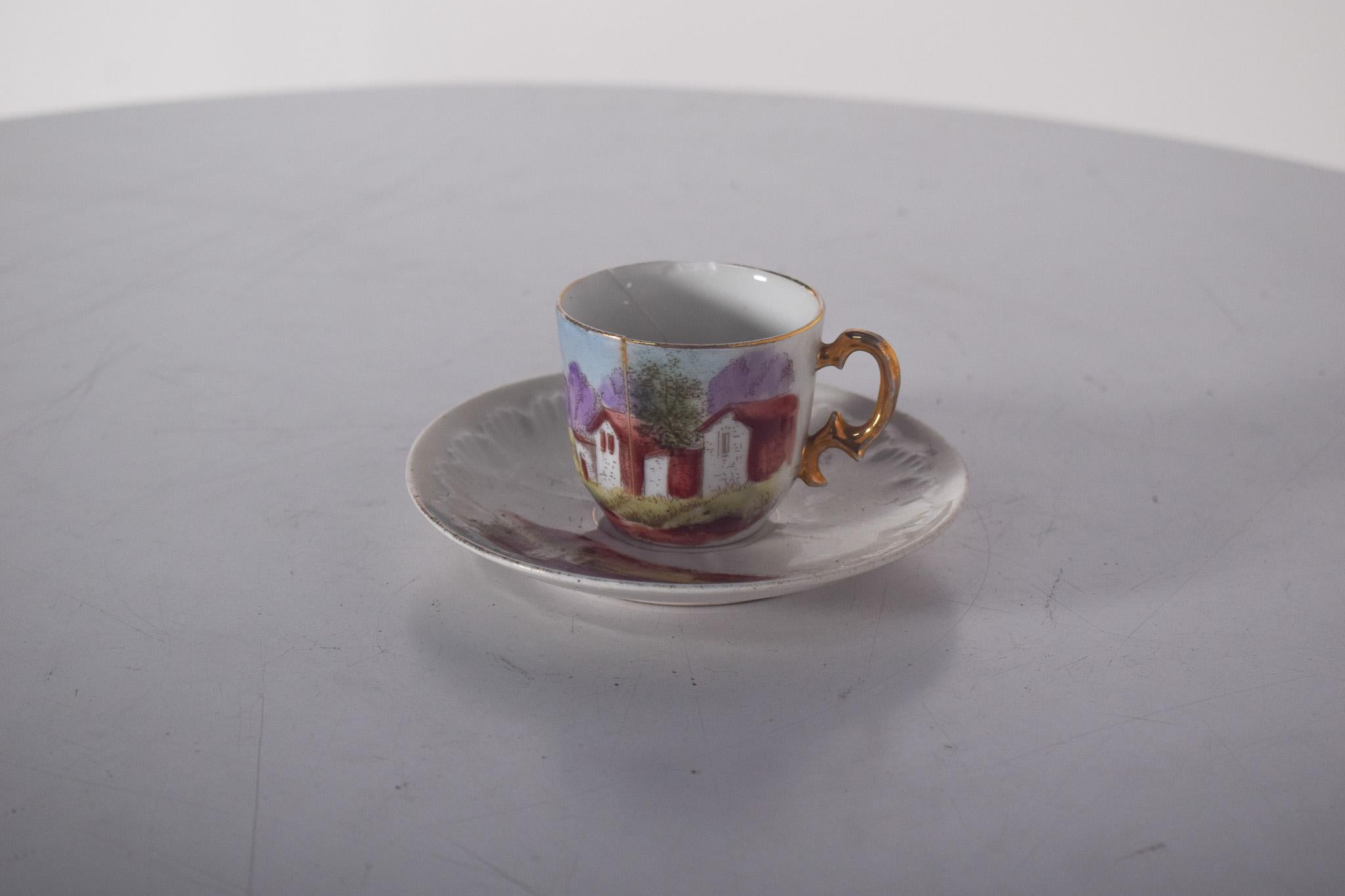 Tasse et soucoupe en porcelaine de Limoges. Décoré d'un paysage rural avec des maisons rustiques, des arbres et des montagnes en arrière-plan. Les couleurs vives du décor se détachent sur le fond blanc de la porcelaine, créant un effet visuel