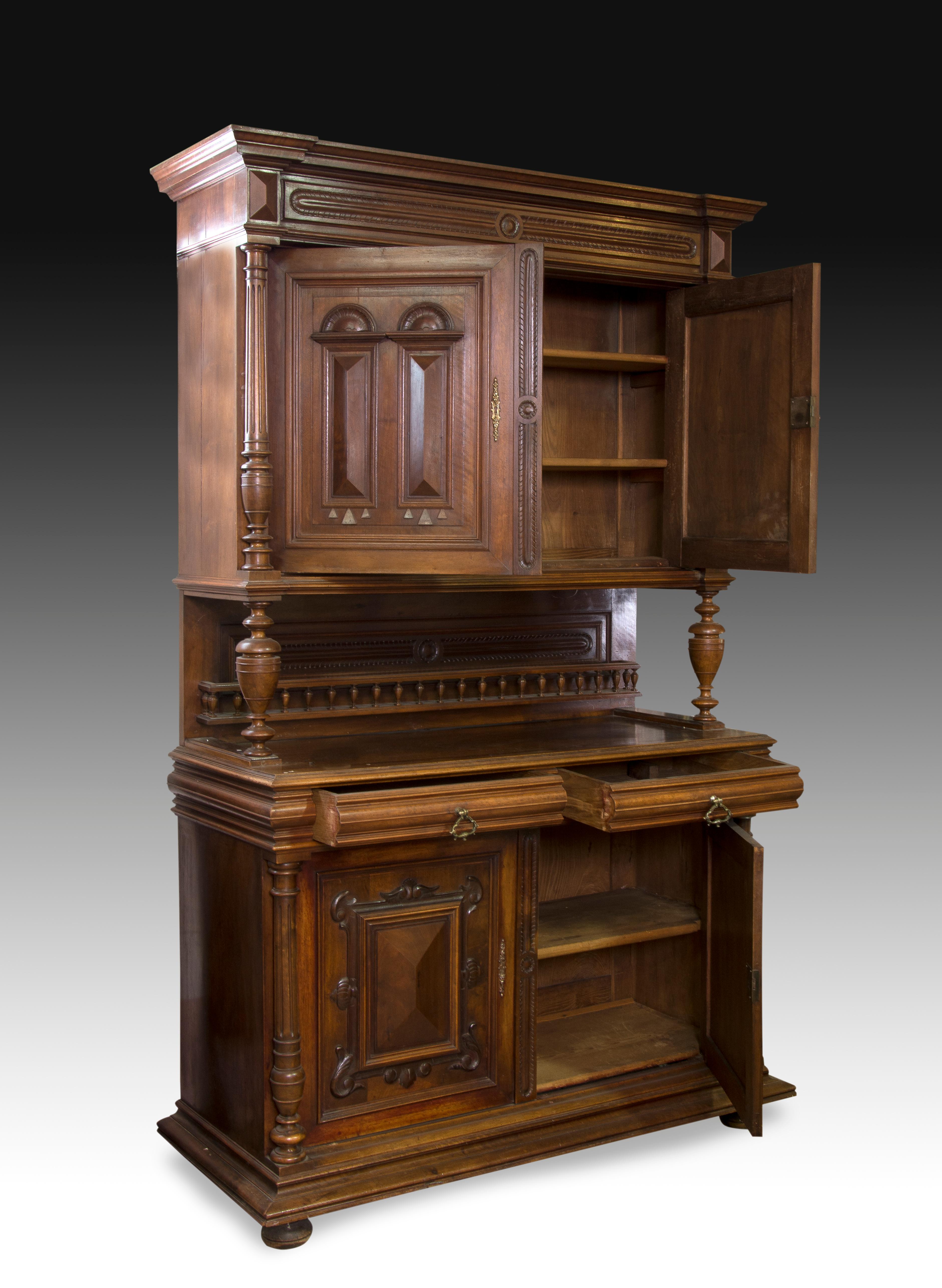 Double body cupboard with decorated front made of carved walnut wood. The lower body has a decoration on both doors, enhanced with columns on the sides; Similar composition is found in the upper body, varying the decorative theme of the doors. In