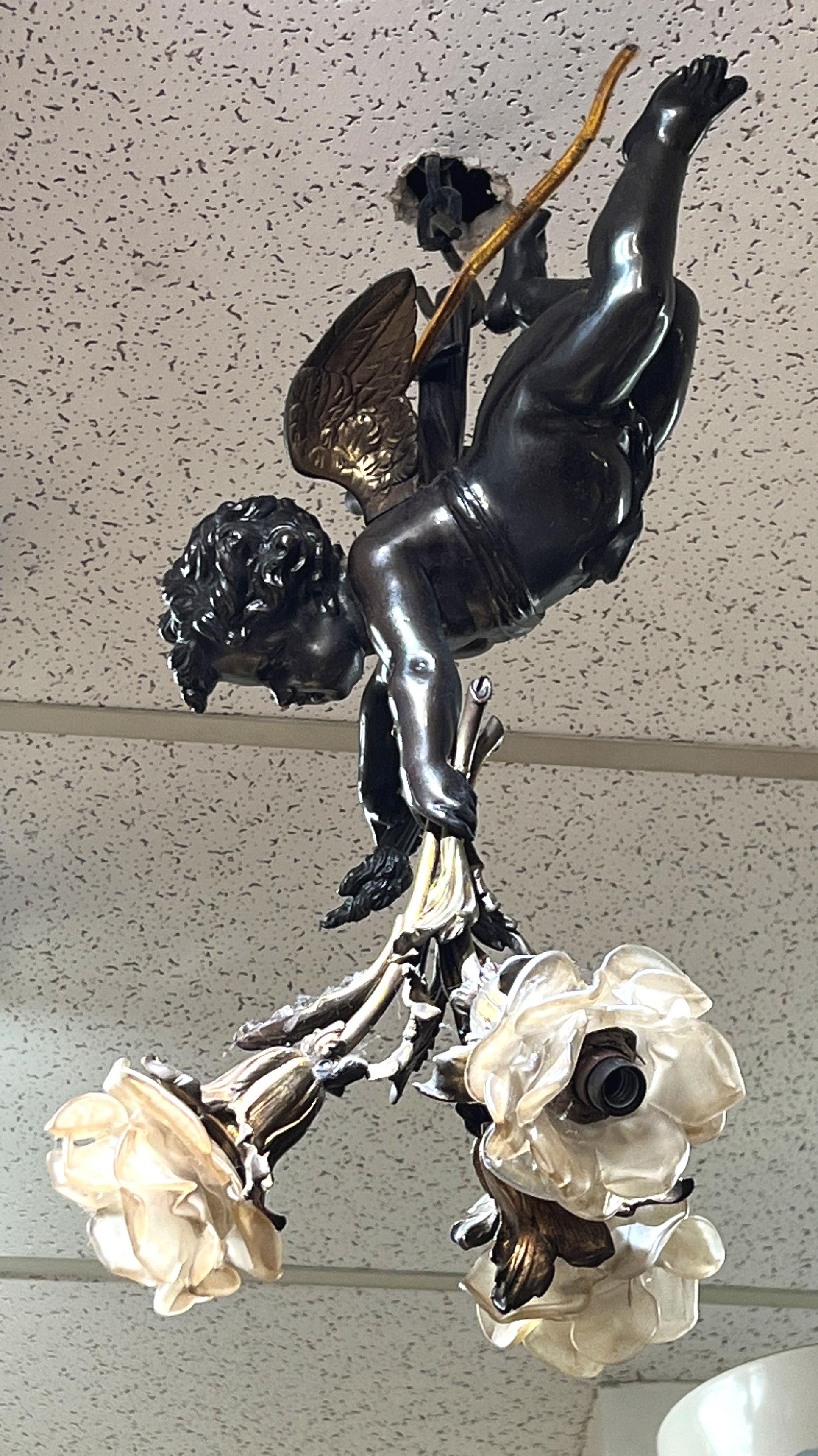 Our antique gilt and patinated bronze chandelier depicts Cupid ln flight and features three candelabra size light sockets with molded glass shades. Partial wiring.