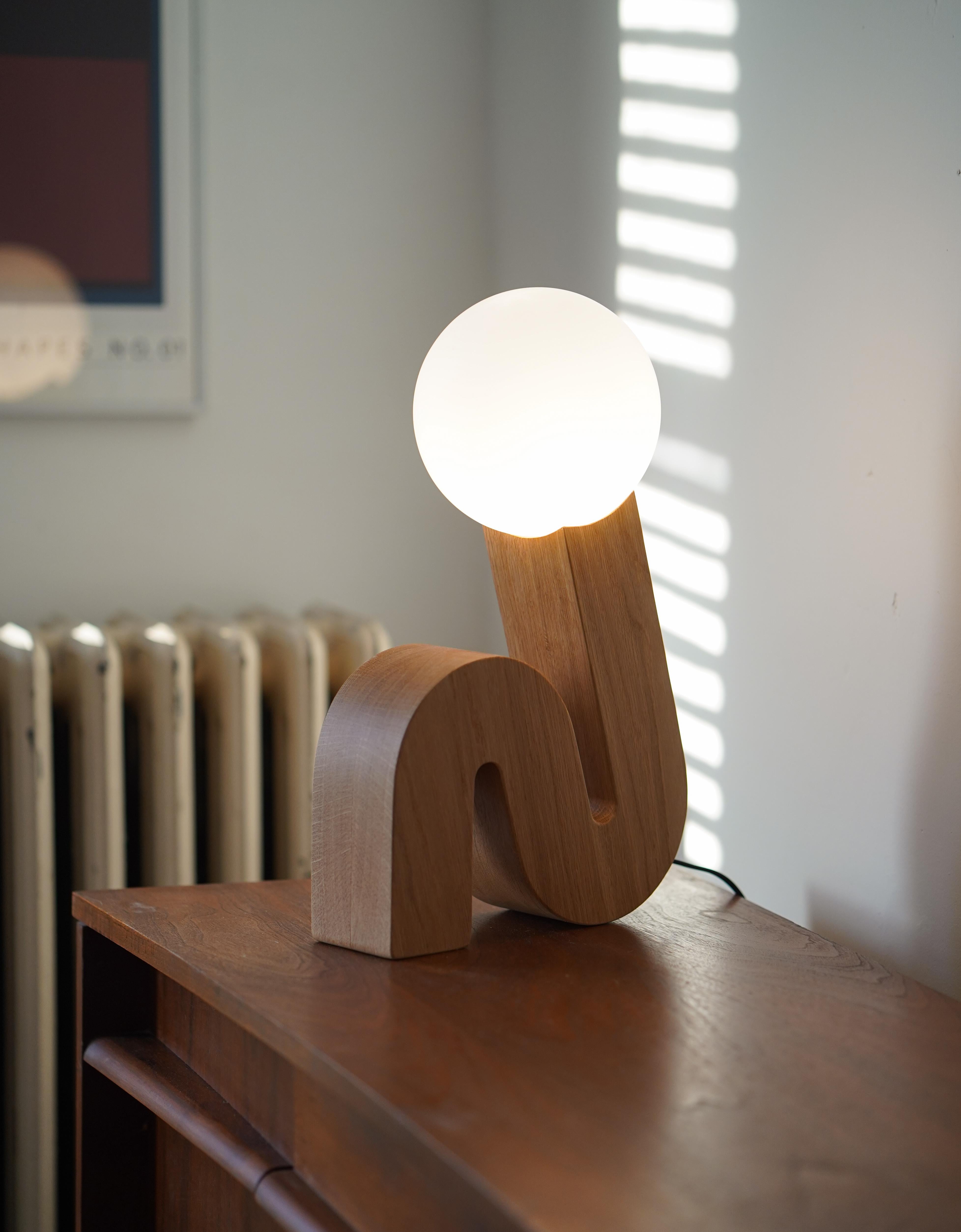 A lamp that is limber. 

Mimicking a sit-up position, the curl lamp uses a spherical glass shade nested into the top of a curved wooden base to resemble a head and body of a person mid-exercise.

The curl lamp is crafted and hand-finished from