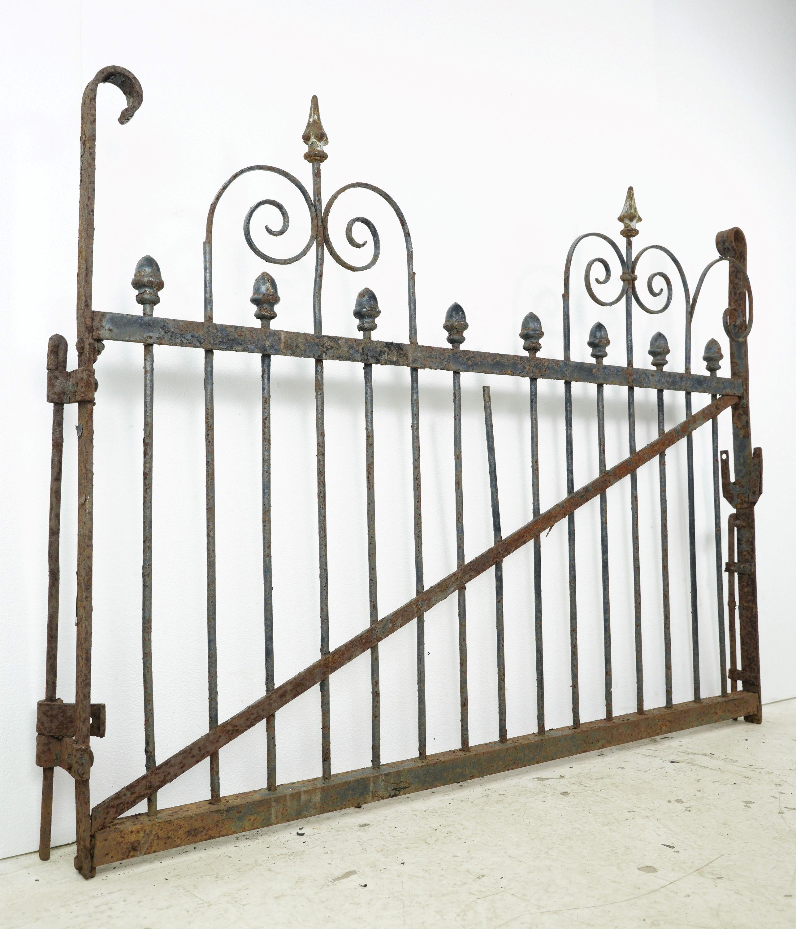 Wrought iron scrolls and cast iron spears and finials make up this charming gate. Install it as a stylish decorative piece or as a functional privacy barrier. This is in fair condition, with surface wear and missing elements. Many iron gates can be