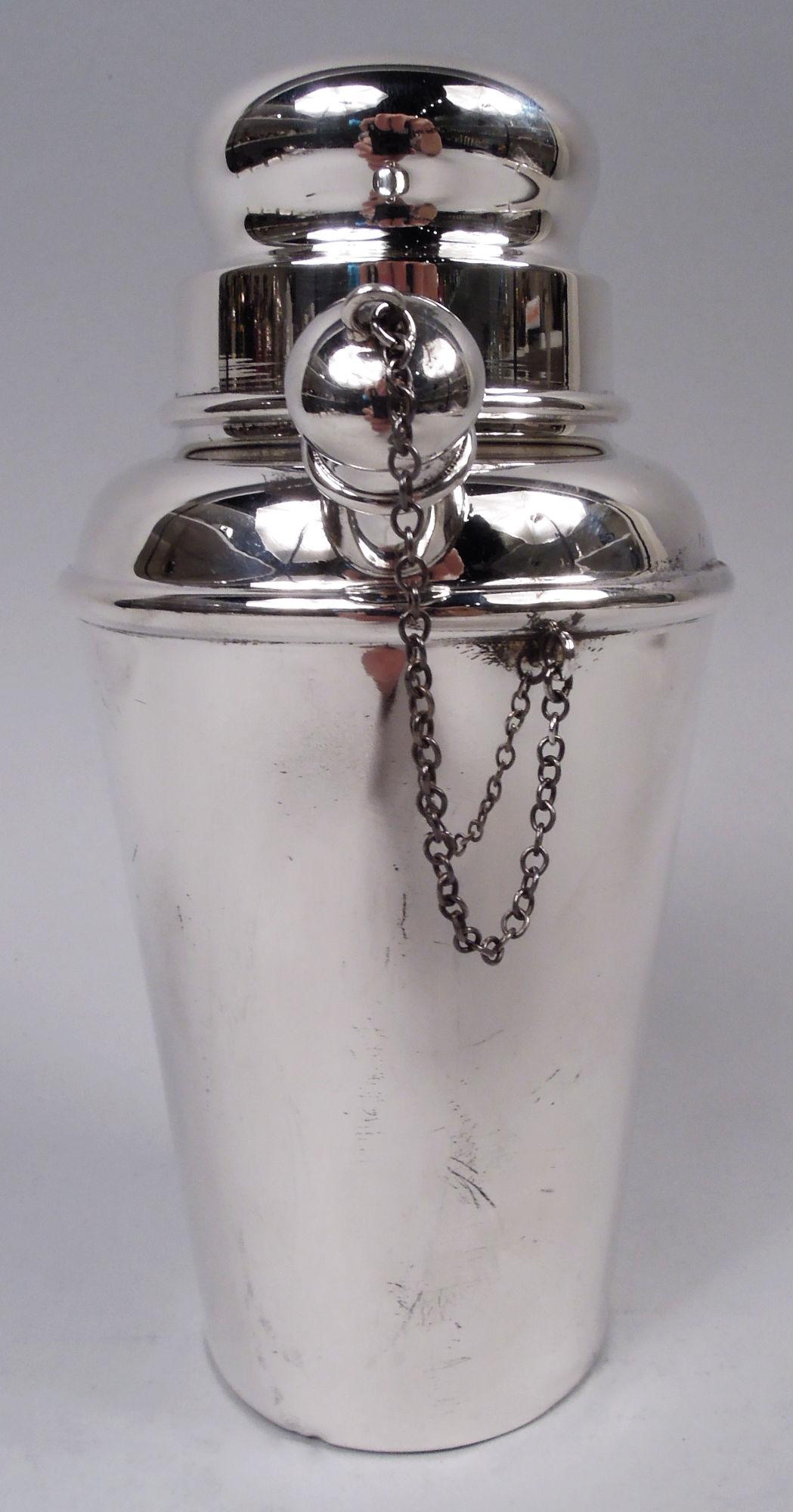 Modern sterling silver mini martini shaker, ca 1930. Straight and tapering sides, curved shoulder, and short neck with snug-fitting bun cover. Spout diagonal with chained ball cap for secure shaking. Handy small size for stylish solo drinking. Fully