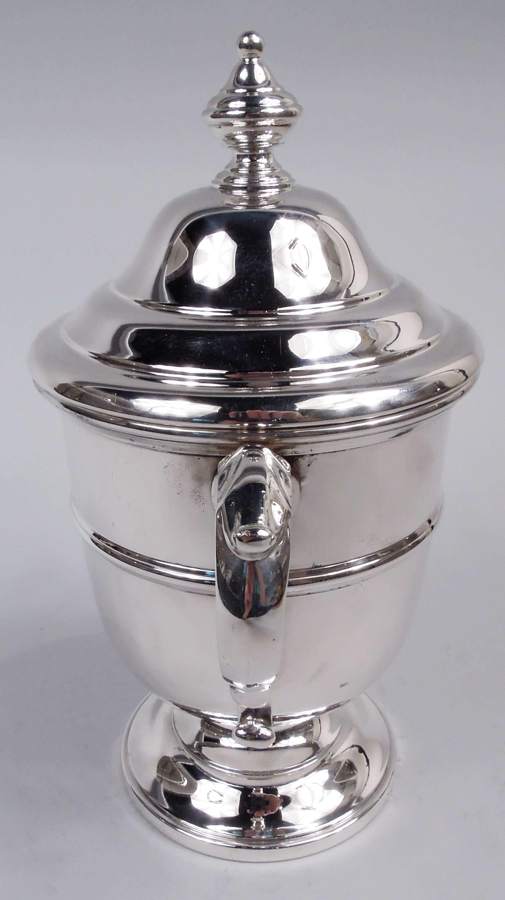 Urna classica in argento sterling. Realizzato da Currier & Roby a New York, nel 1930 circa. Forma tradizionale con cintura e piede a cupola; maniglie laterali a doppio scorrimento con cappuccio a foglia. Coperchio a cupola con terminale vasiforme.