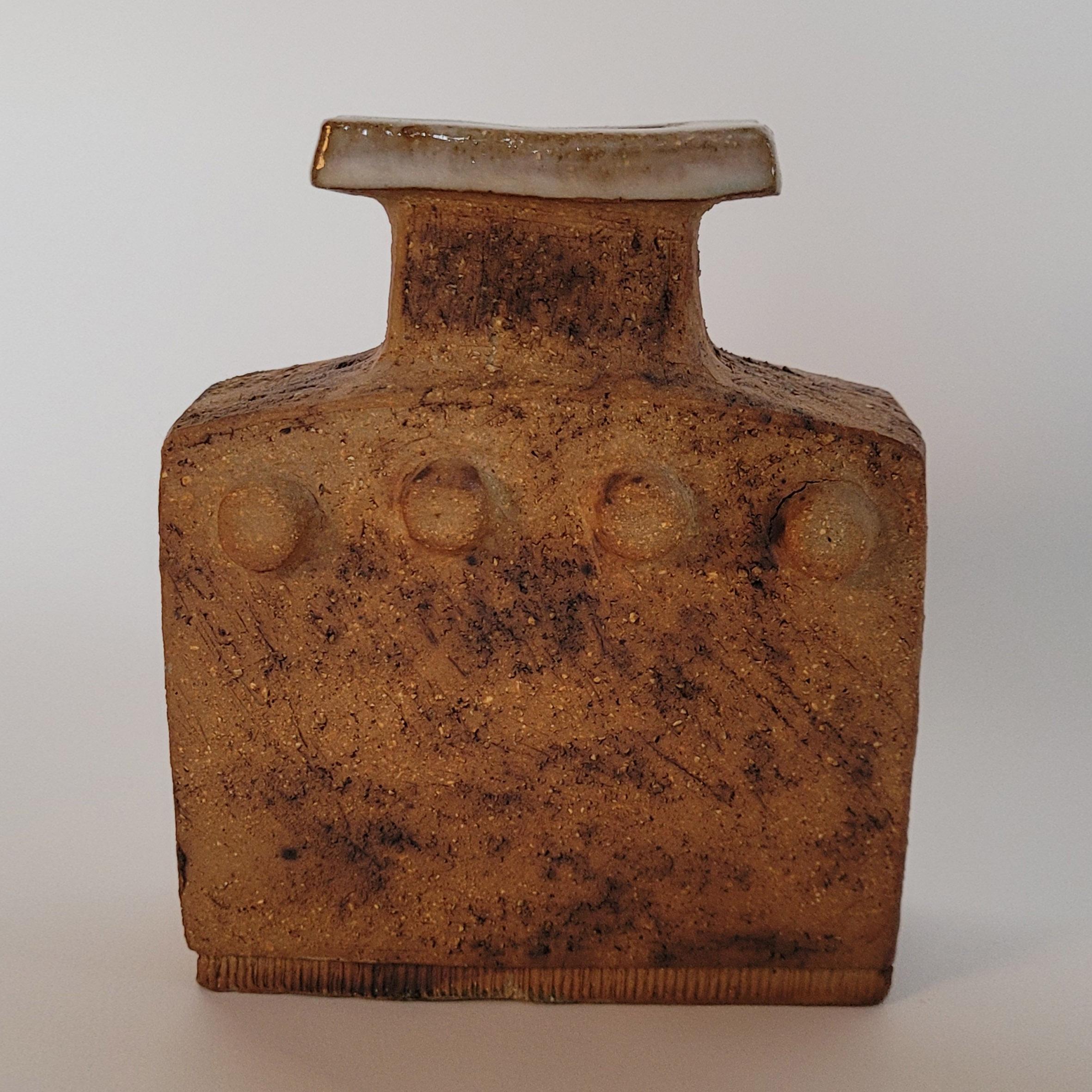 Curt Magnus Addin (1931-2007)

Kleine Vase

Eine flaschenförmige Vase aus Steinzeug mit rechteckigem Korpus, der auf jeder Seite mit vier Punkten verziert ist, darüber ein gestreckter Hals mit glasiertem Rand.
Signiert unter 