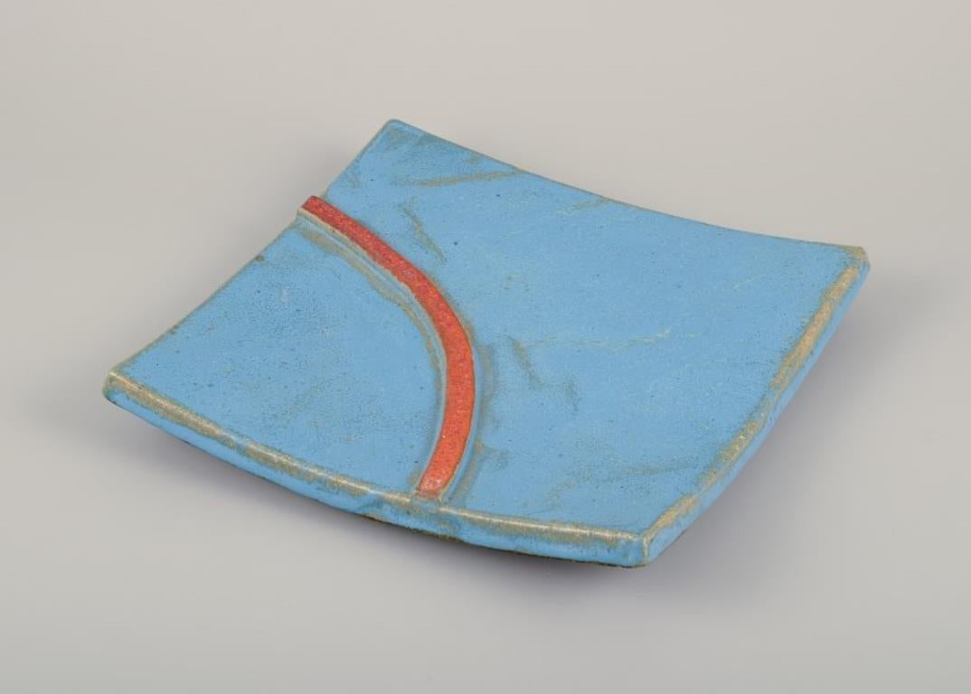 Curt Magnus Addin (1931-2007), ceramista sueco.
Exclusiva bandeja cuadrada de cerámica de estilo modernista. 
De arcilla grog con vidriado turquesa y una línea naranja.
De los años setenta.
Firmado.
En perfecto estado.
Dimensiones: Diámetro 27,0 cm