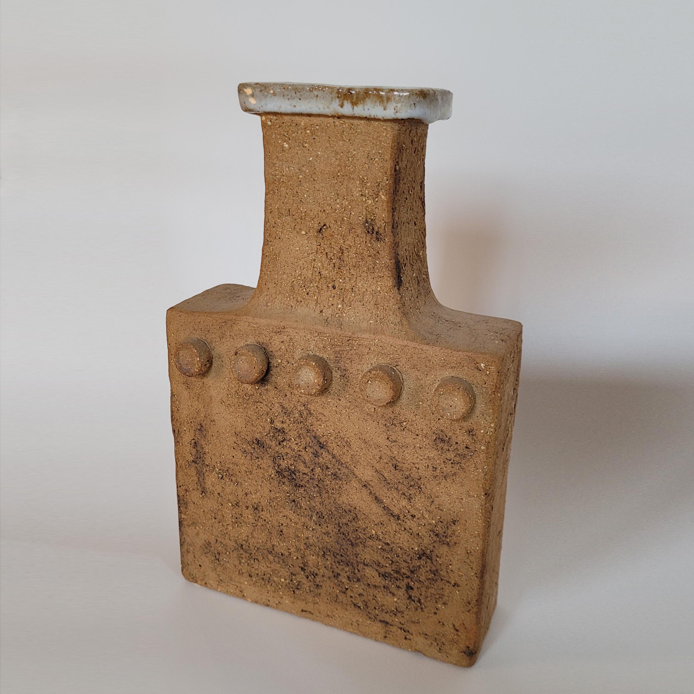 Curt Magnus Addin (1931-2007)

Große Vase

Eine flaschenförmige Vase aus Steinzeug mit rechteckigem Korpus, der auf jeder Seite mit fünf Punkten verziert ist, darüber ein gestreckter Hals mit glasiertem Rand.
Unten zweimal gestempelt 