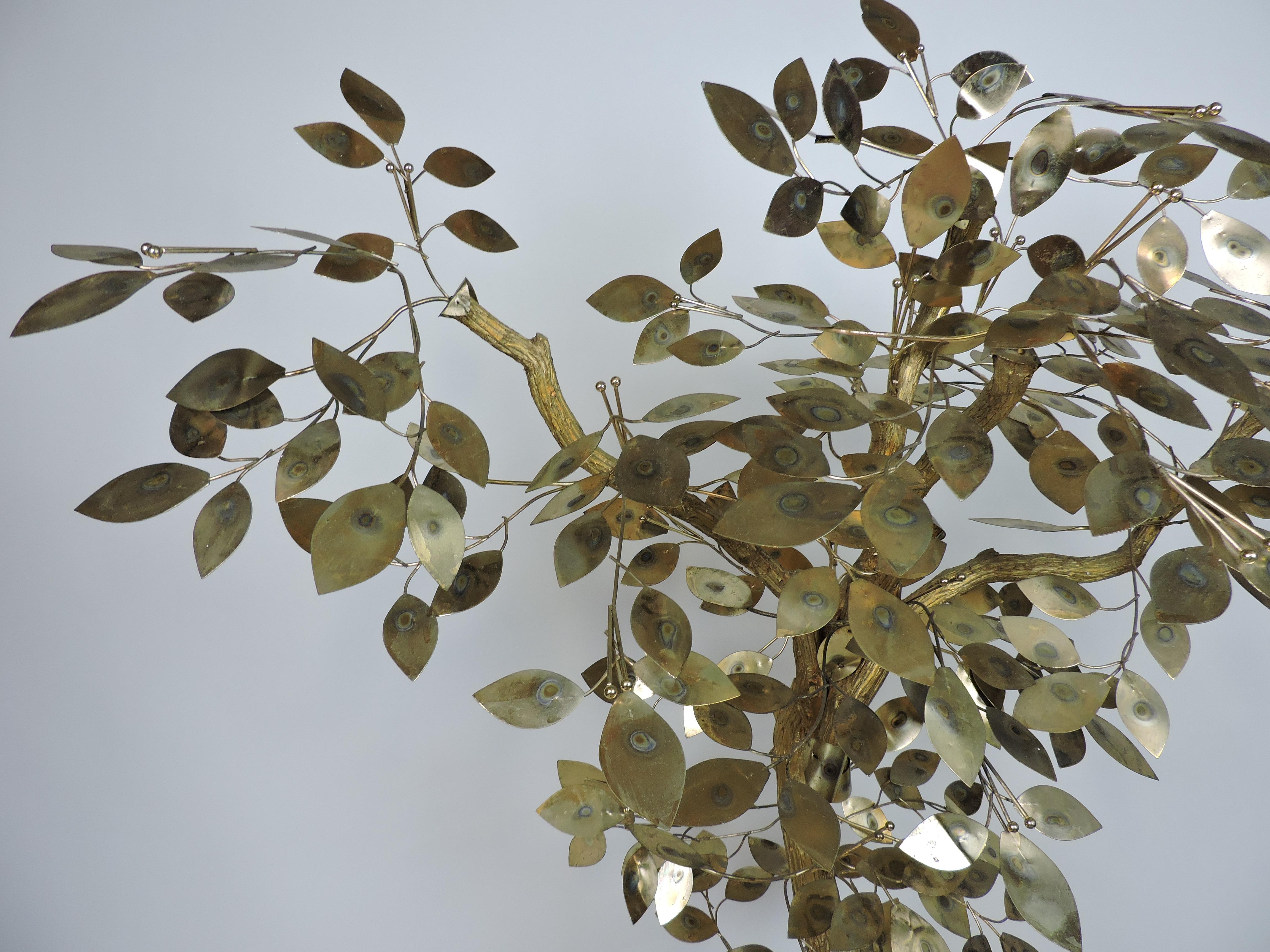 Large and striking brass tree sculpture attributed to Curtis Jere. This floor piece has metal leaves attached to a painted natural wood tree trunk. It sits in a gold tone container, the top of which is covered with tree bark chips. A beautiful
