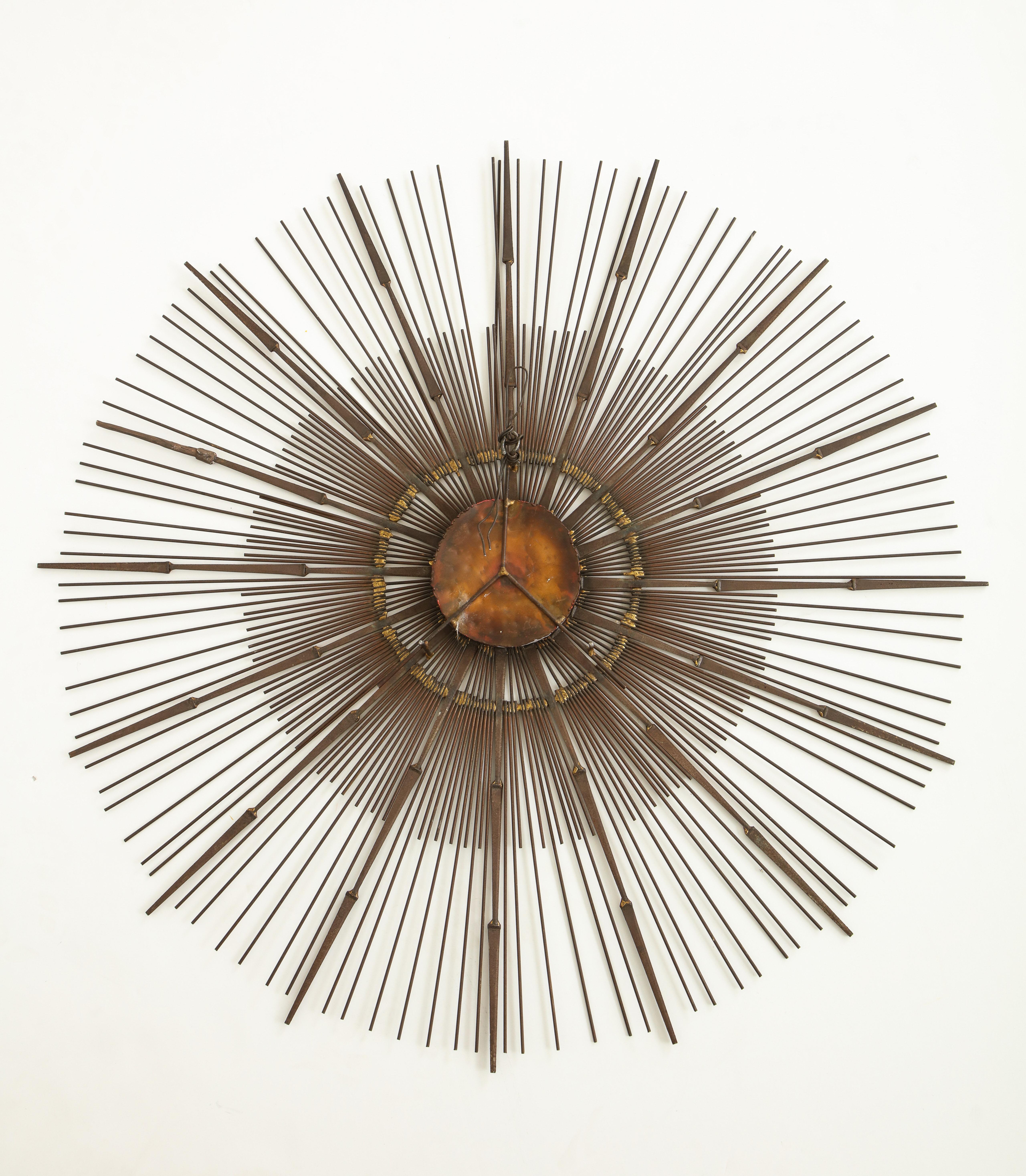 Brass wall sunburst sculpture by Curtis Jere, having one tier of rounded rods and one tier of pointed rods radiating around a central copper disc.